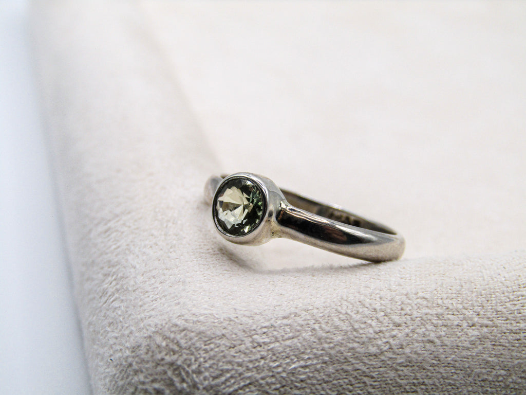 Silver ring with a green gemstone on a textured white surface