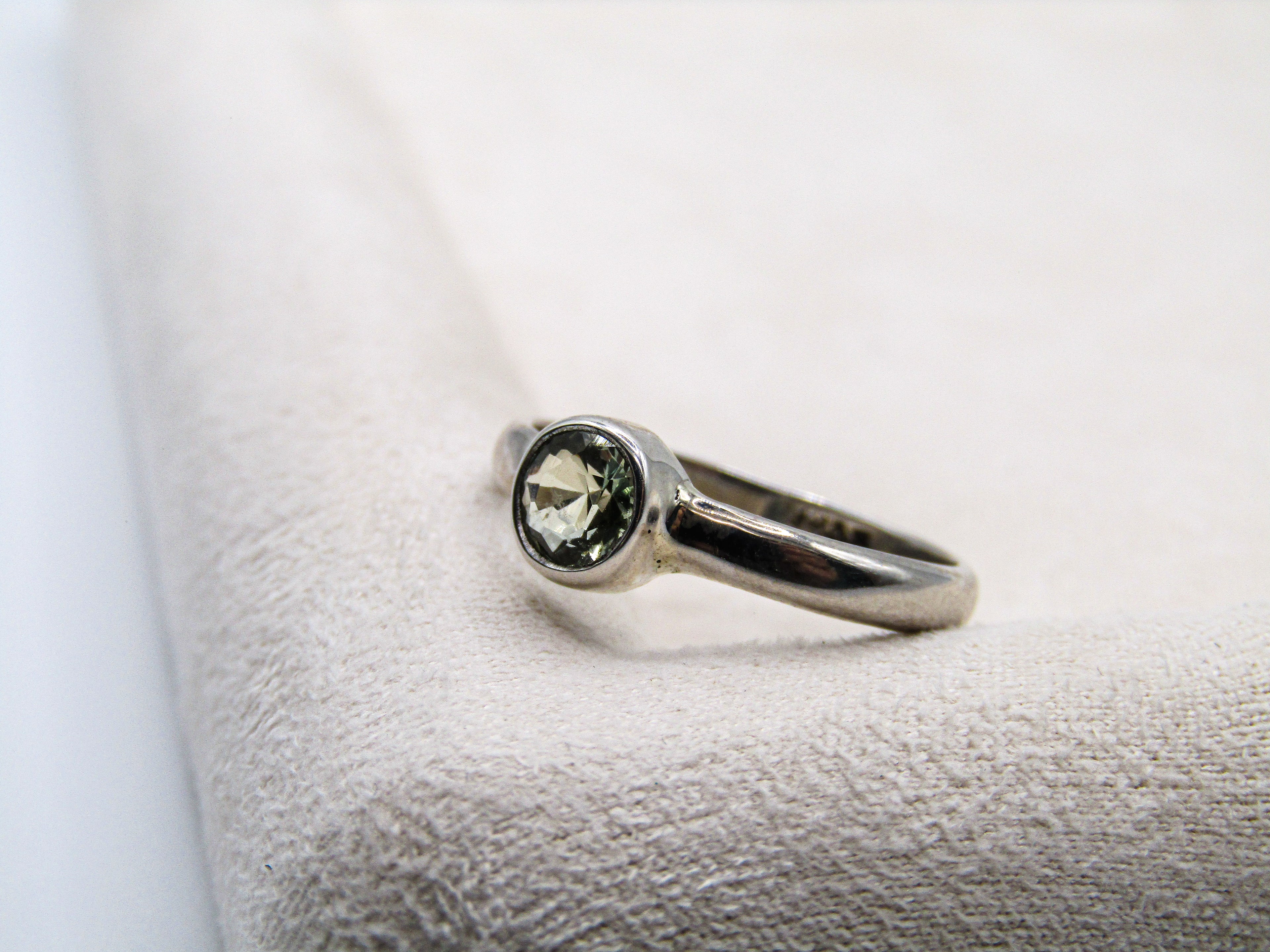 Silver ring with a green gemstone on a textured white surface