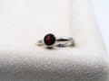 Silver ring with a red gemstone on a white cushion