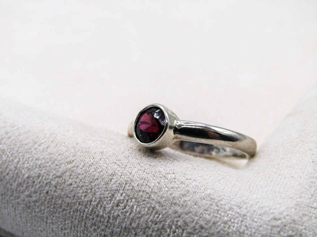 Silver ring with a red gemstone on a white cushion