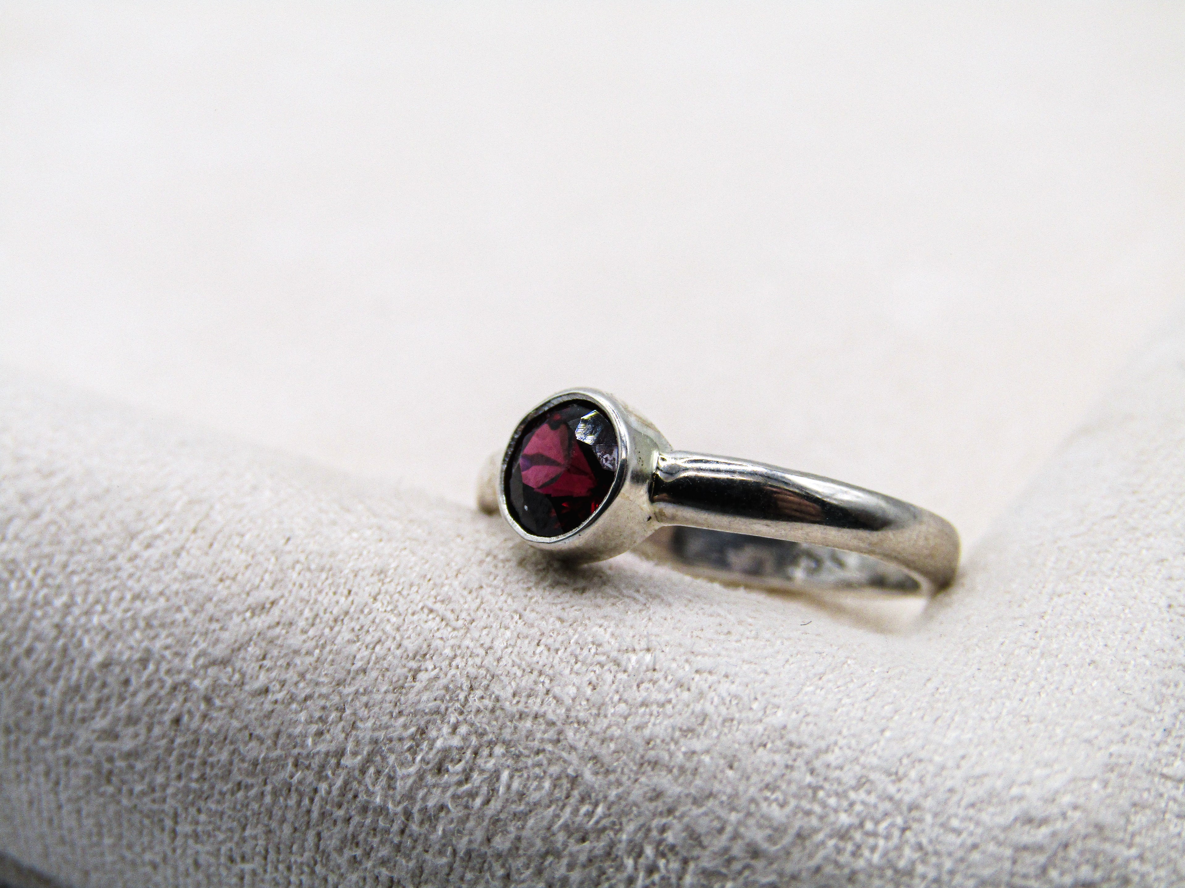 Silver ring with a red gemstone on a white cushion