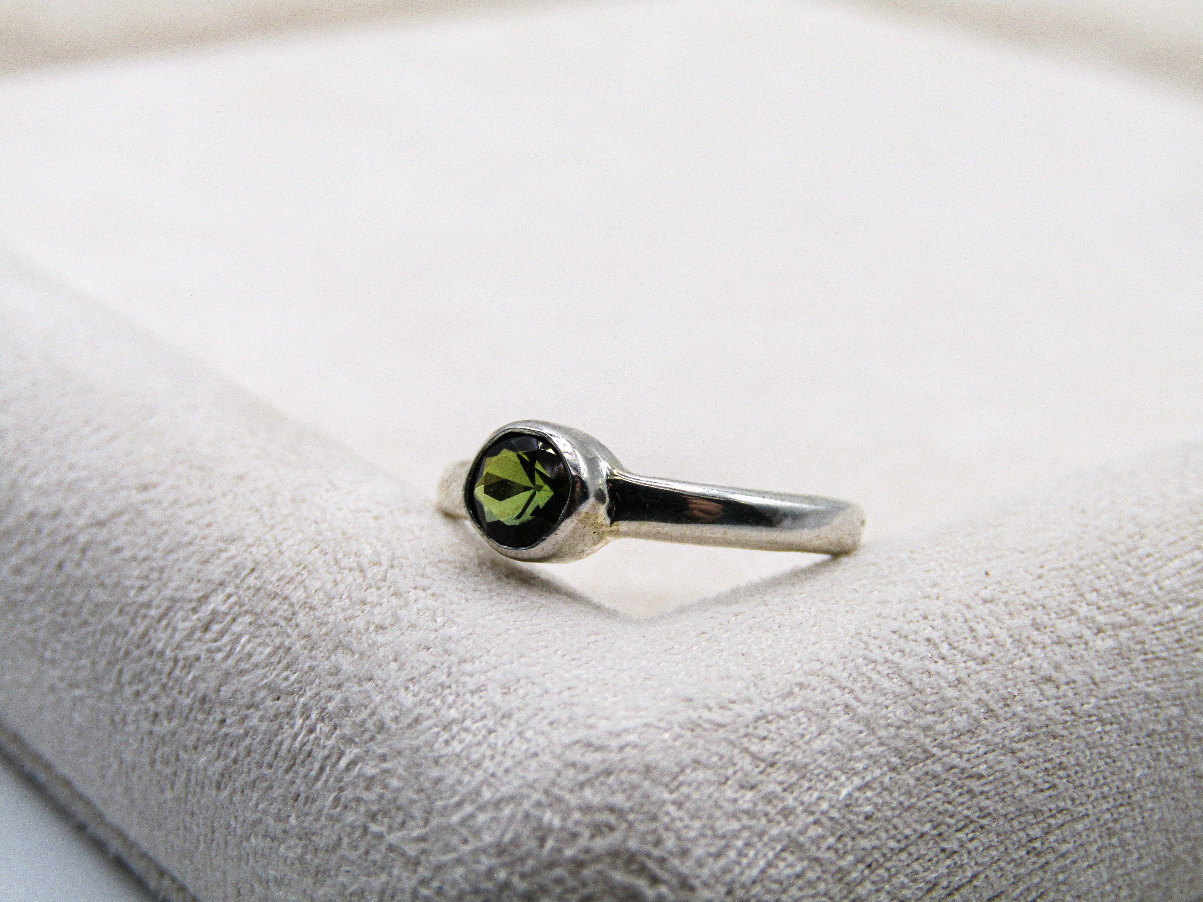 Silver ring with a green gemstone on a textured white surface