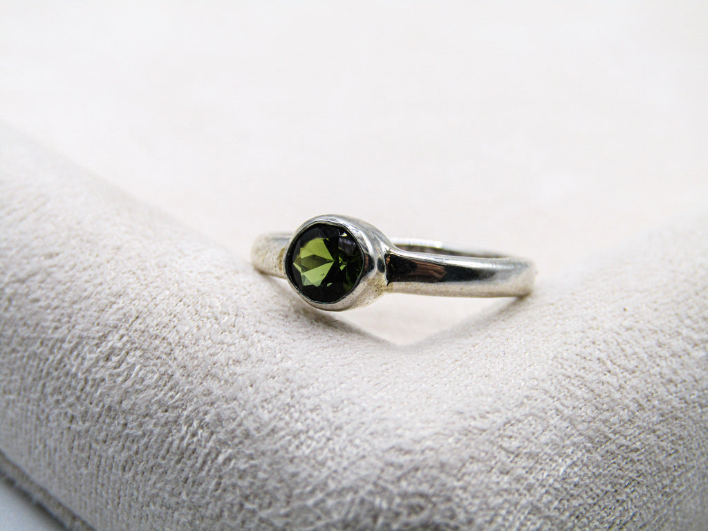 Silver ring with a green gemstone on a textured white surface