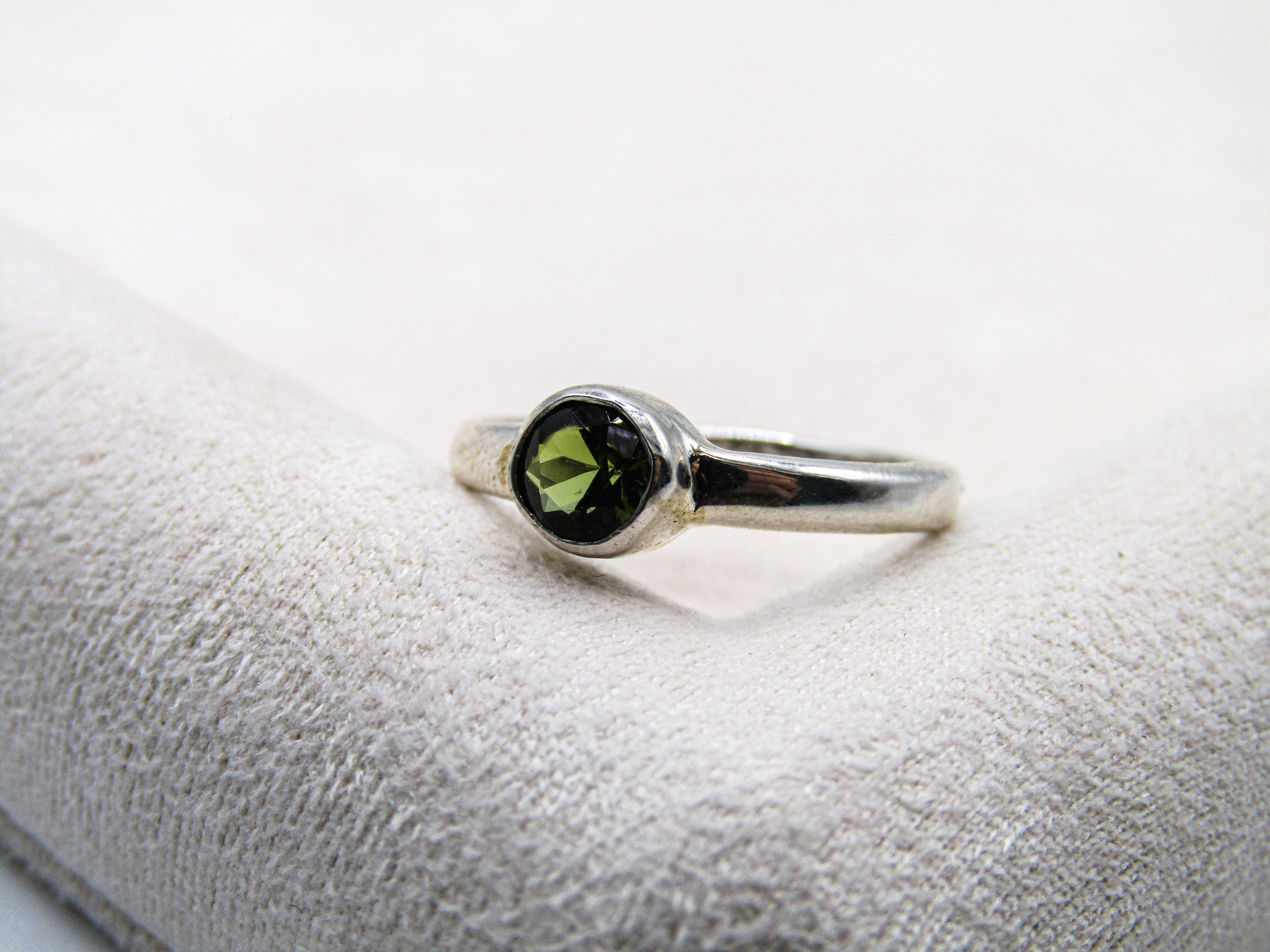 Silver ring with a green gemstone on a textured white surface