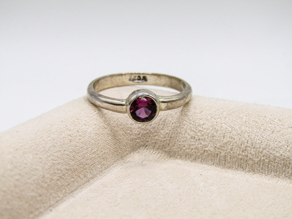 Silver ring with a red gemstone on a beige cushion