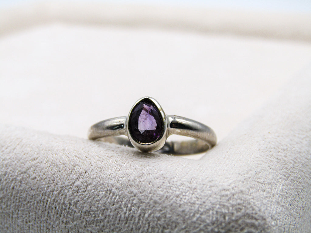 Silver ring with a purple gemstone on a textured white surface