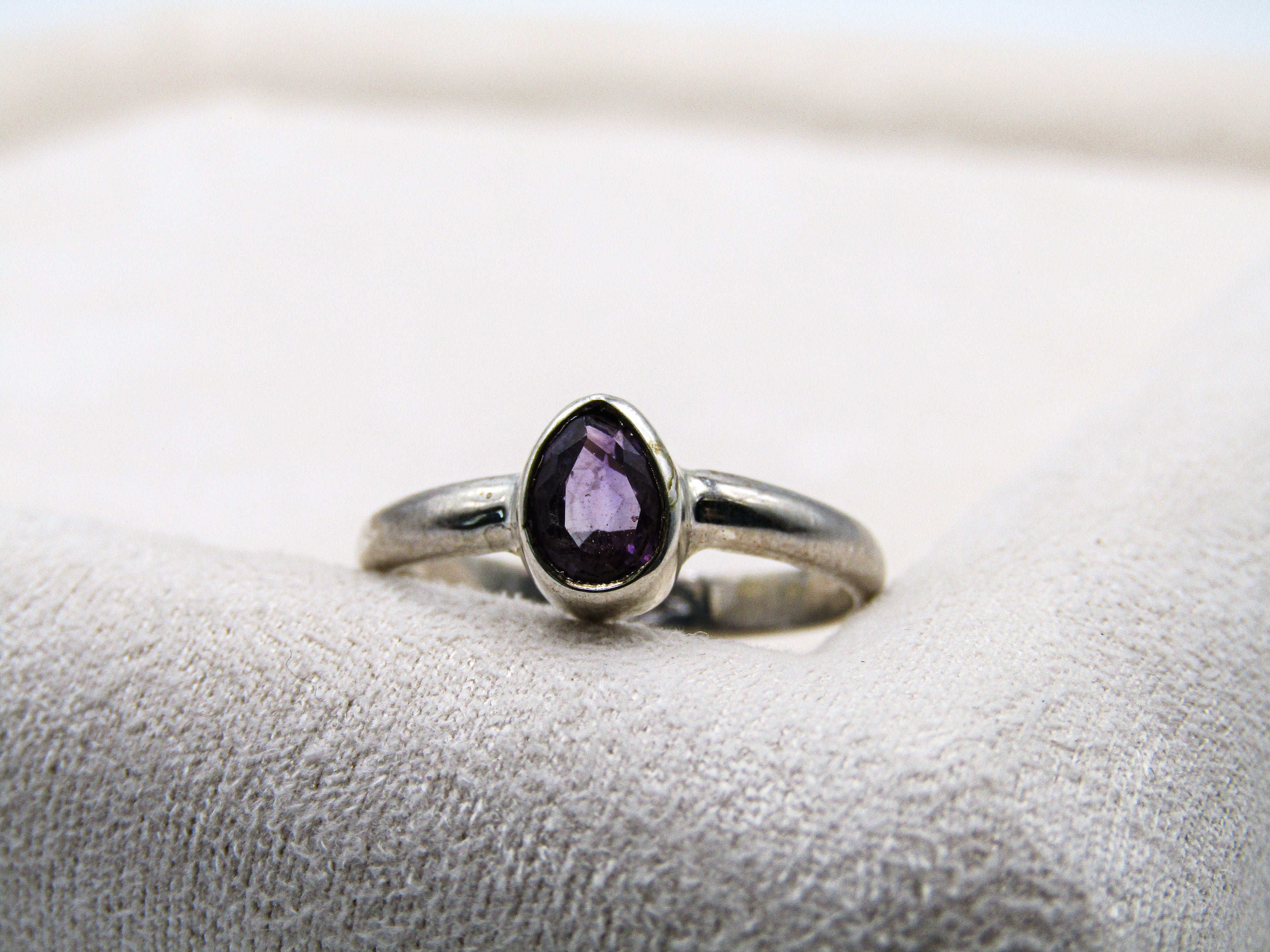 Silver ring with a purple gemstone on a textured white surface