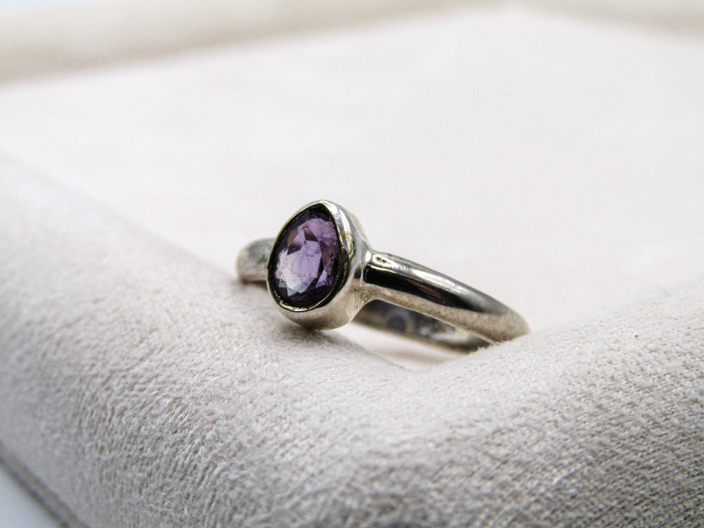 Silver ring with a purple gemstone on a white cushion