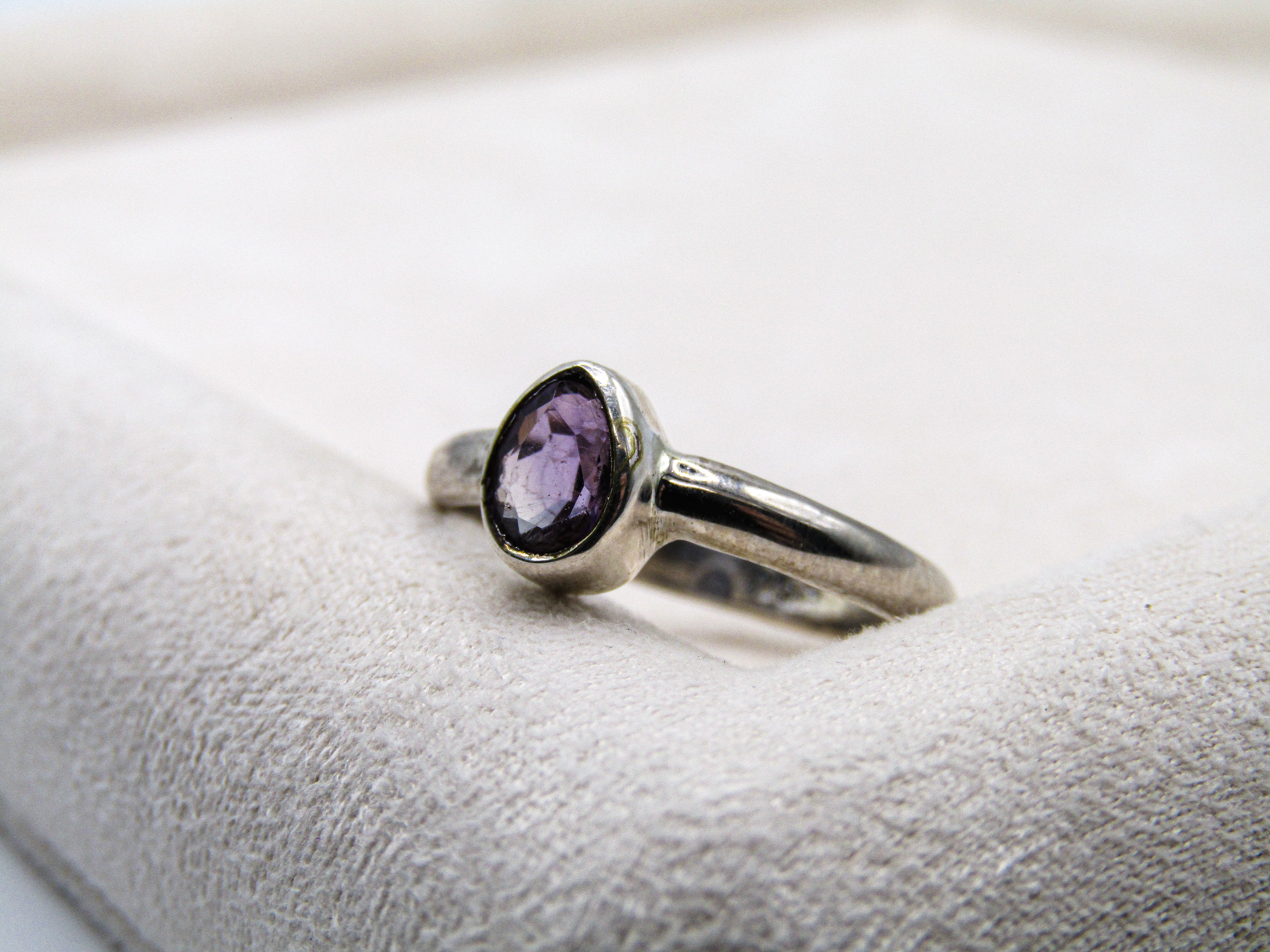 Silver ring with a purple gemstone on a white cushion