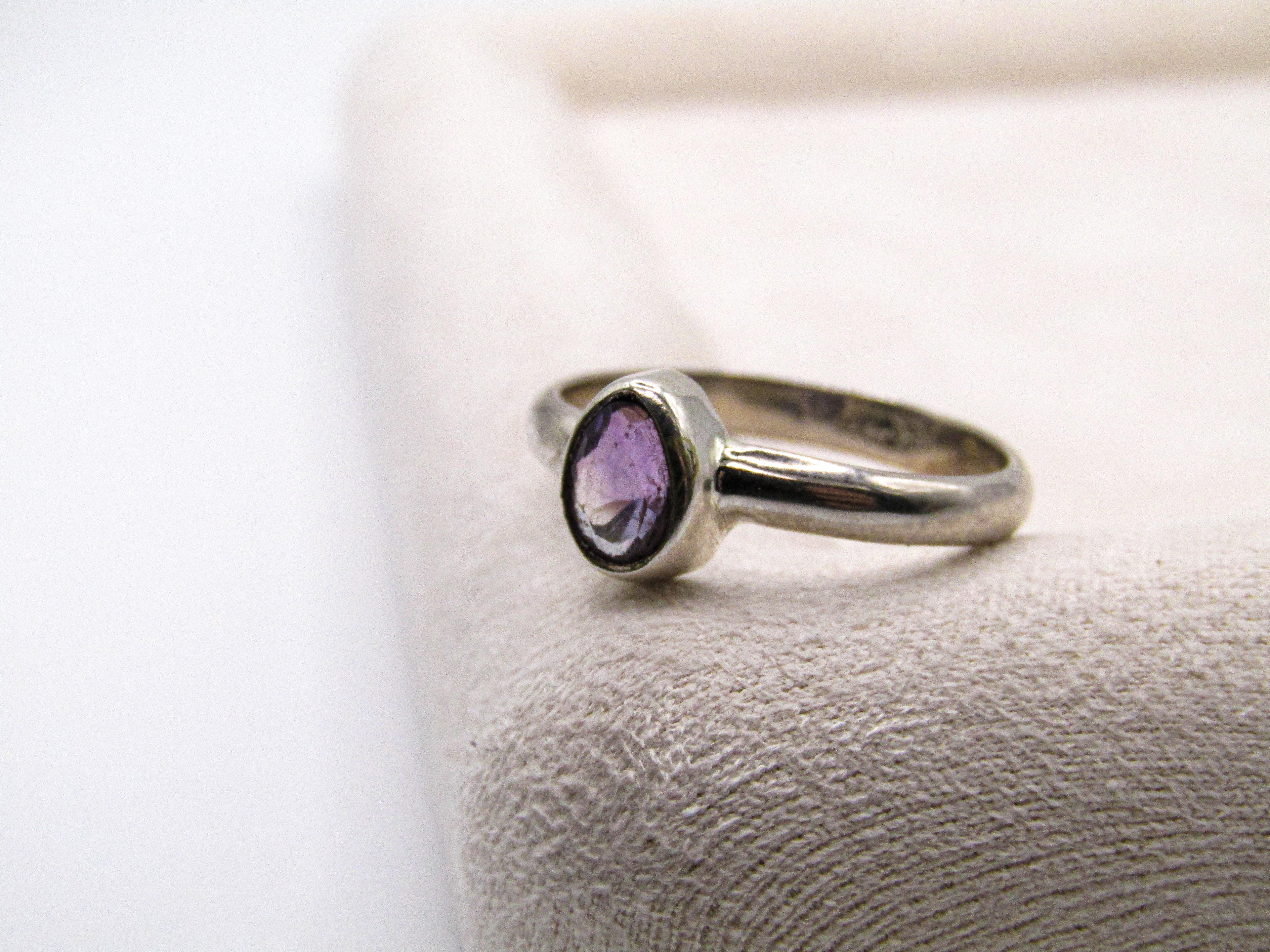 Silver ring with a purple gemstone on a textured surface