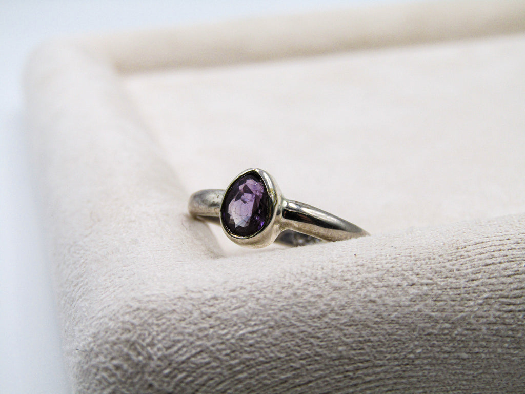 Silver ring with a purple gemstone on a textured surface