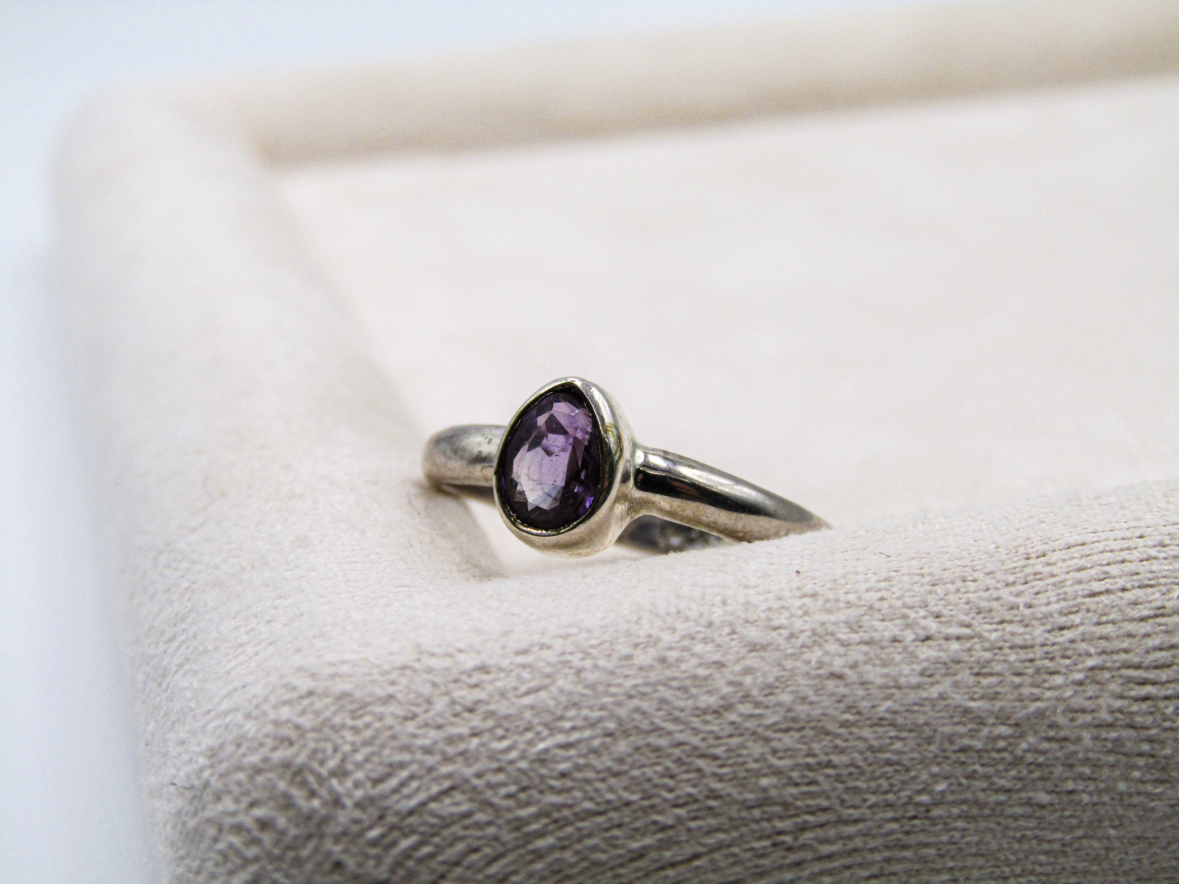 Silver ring with a purple gemstone on a textured surface