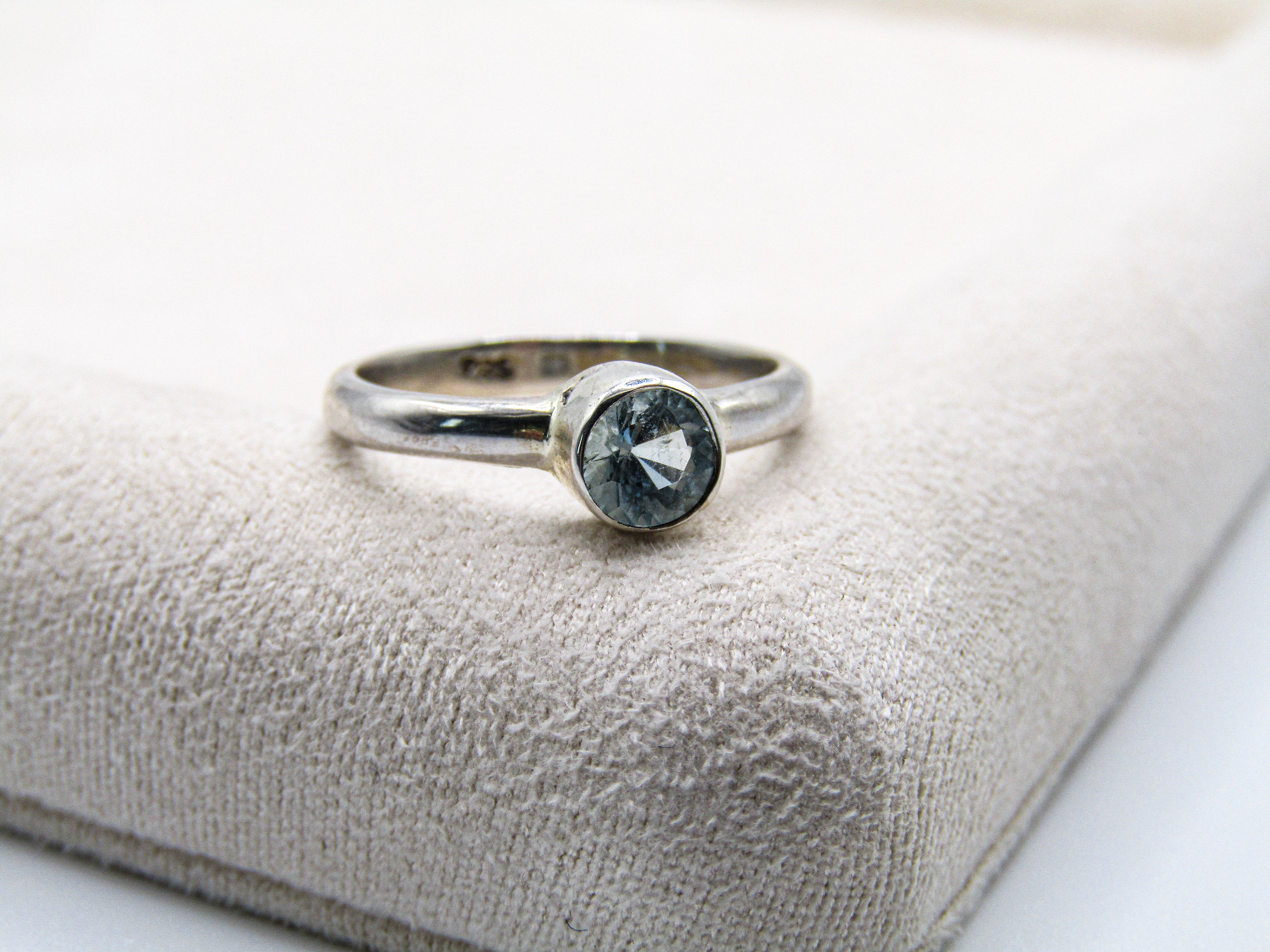 Silver ring with a gemstone on a textured beige surface