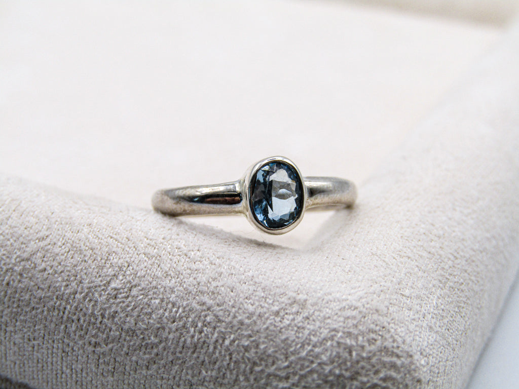 Silver ring with a blue gemstone on a white cushion