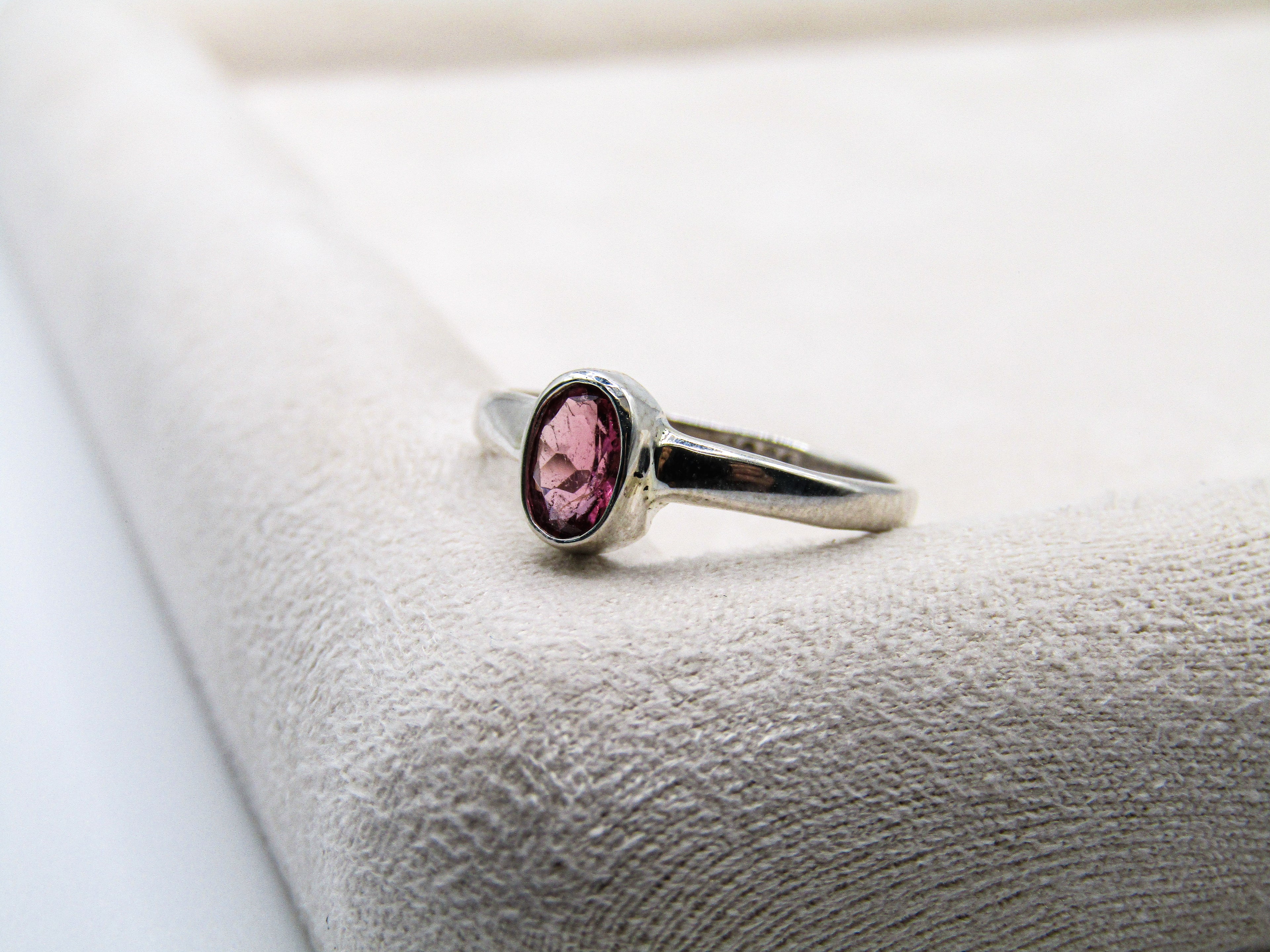 Silver ring with a pink gemstone on a textured white surface