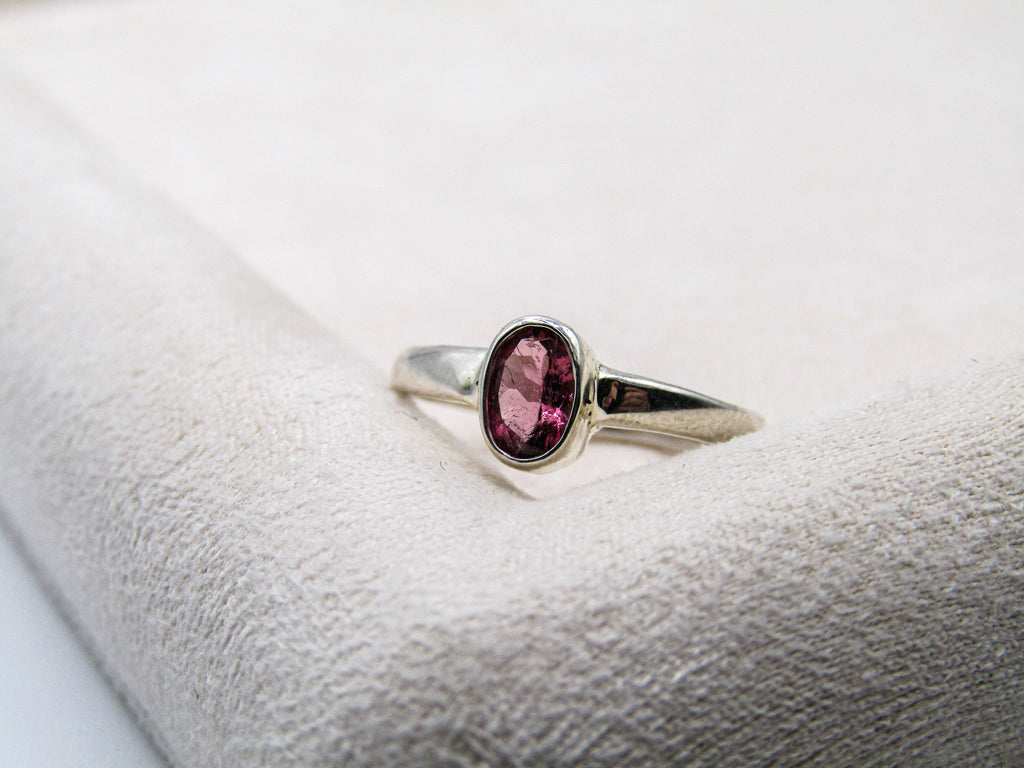 Silver ring with a pink gemstone on a white cushion
