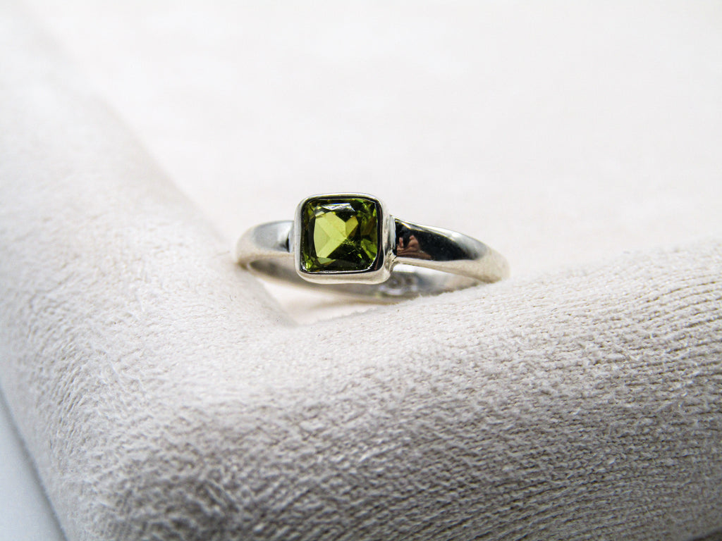 Silver ring with a green gemstone on a white cushion