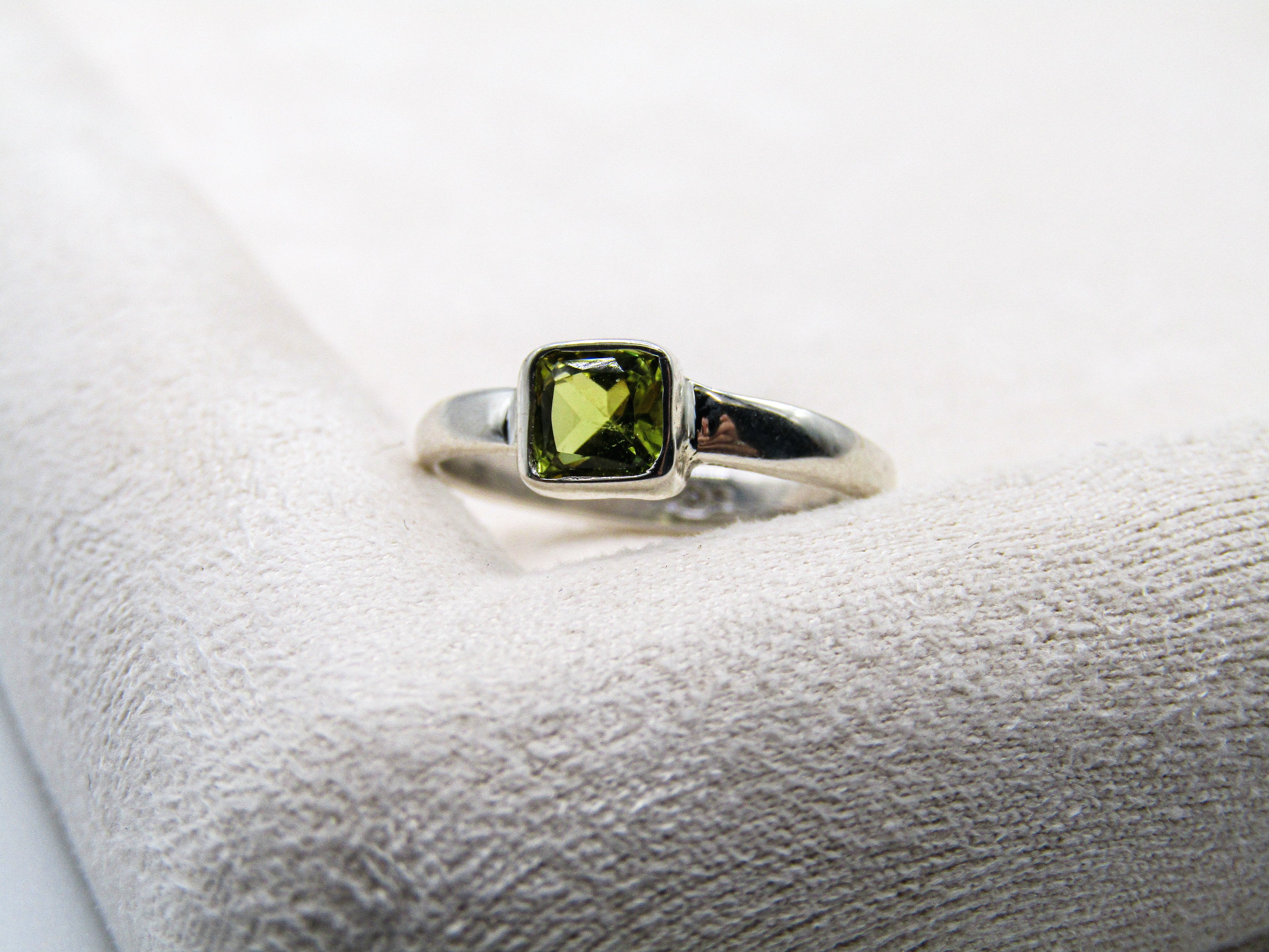 Silver ring with a green gemstone on a white cushion
