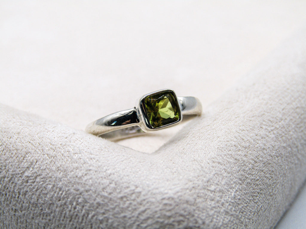 Silver ring with a green gemstone on a white cushion