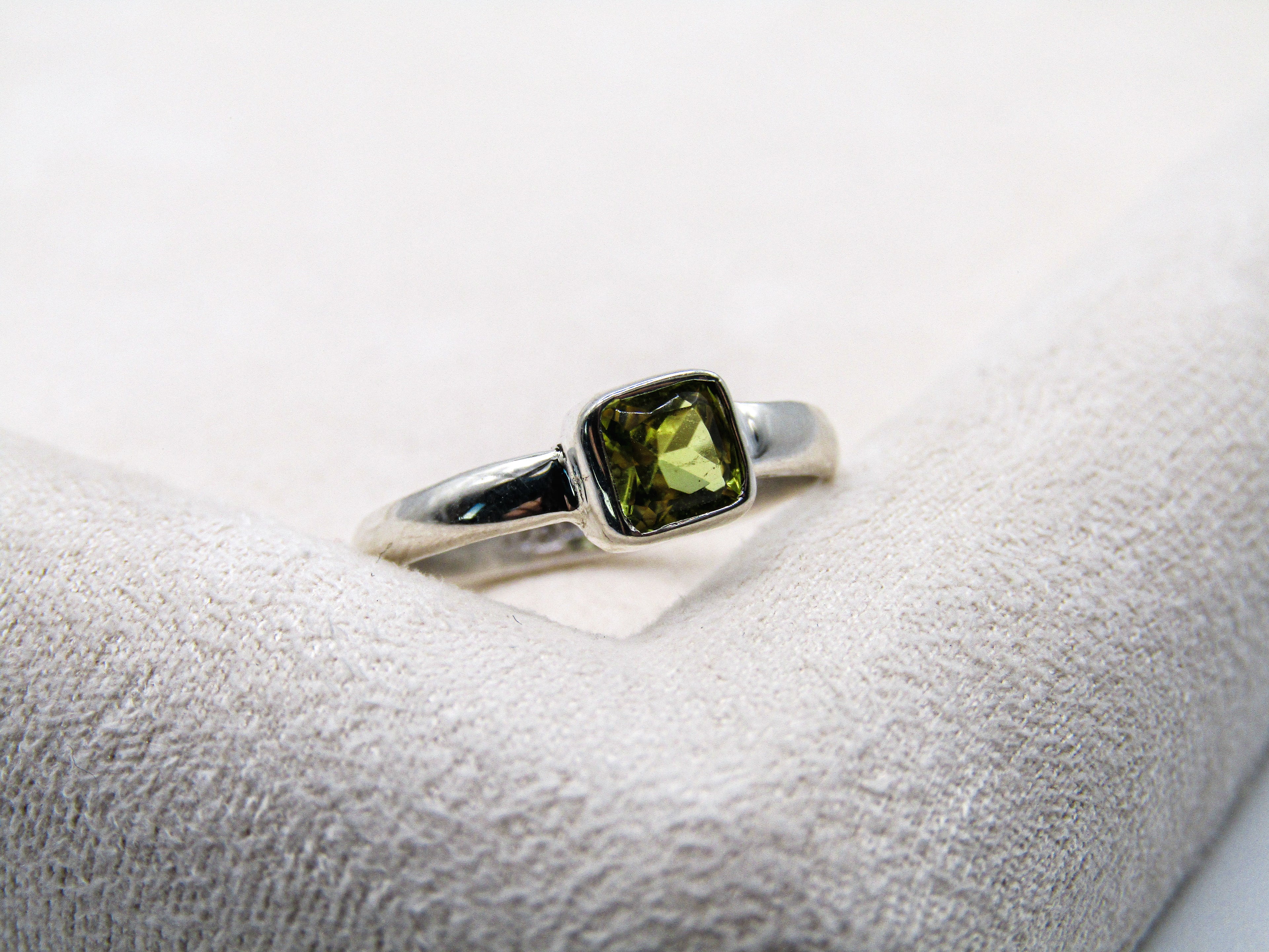 Silver ring with a green gemstone on a white cushion