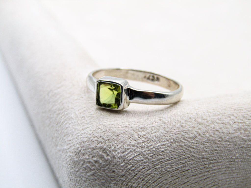 Silver ring with a green gemstone on a textured white surface