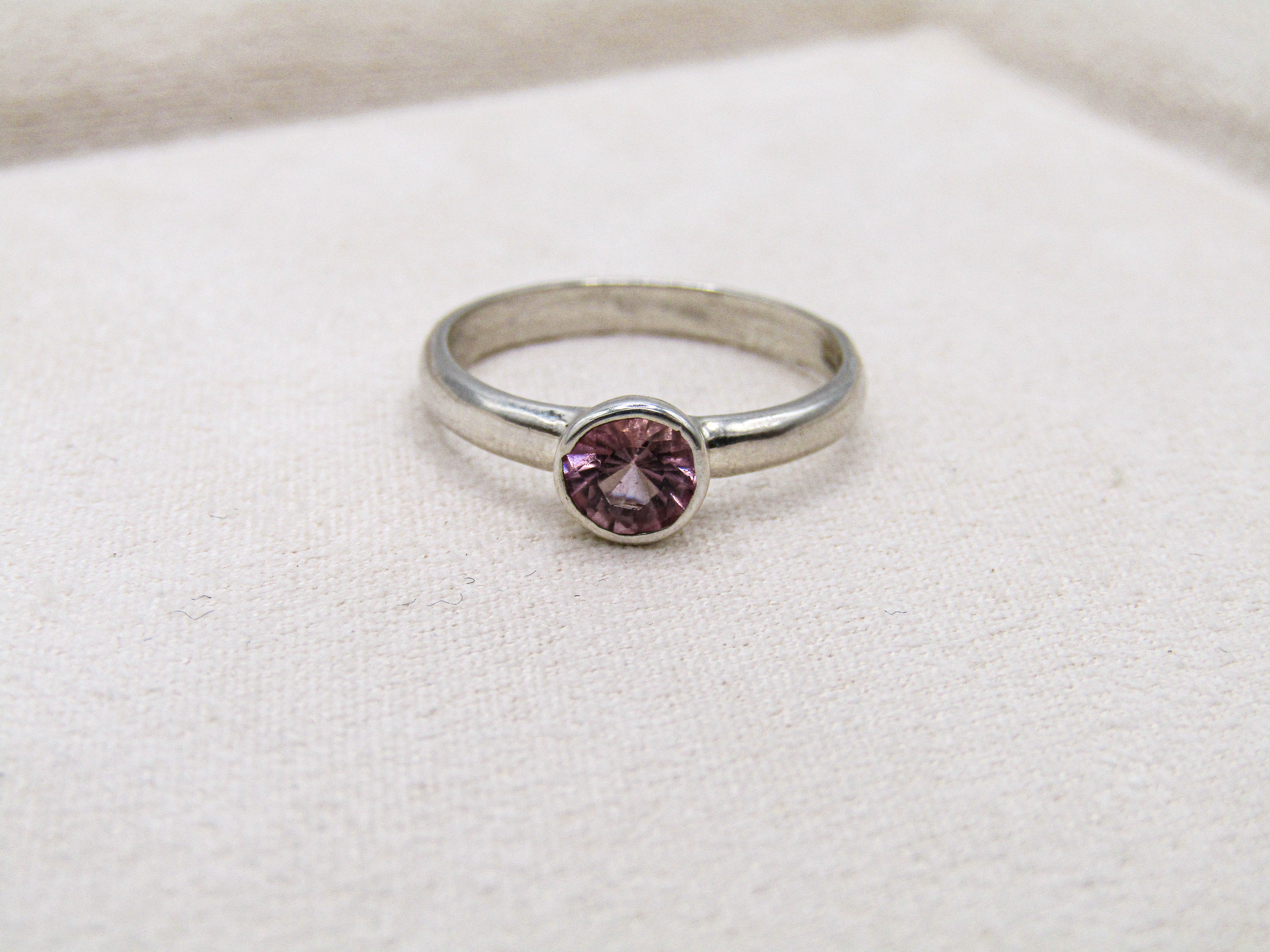 Silver ring with a pink gemstone on a white fabric background