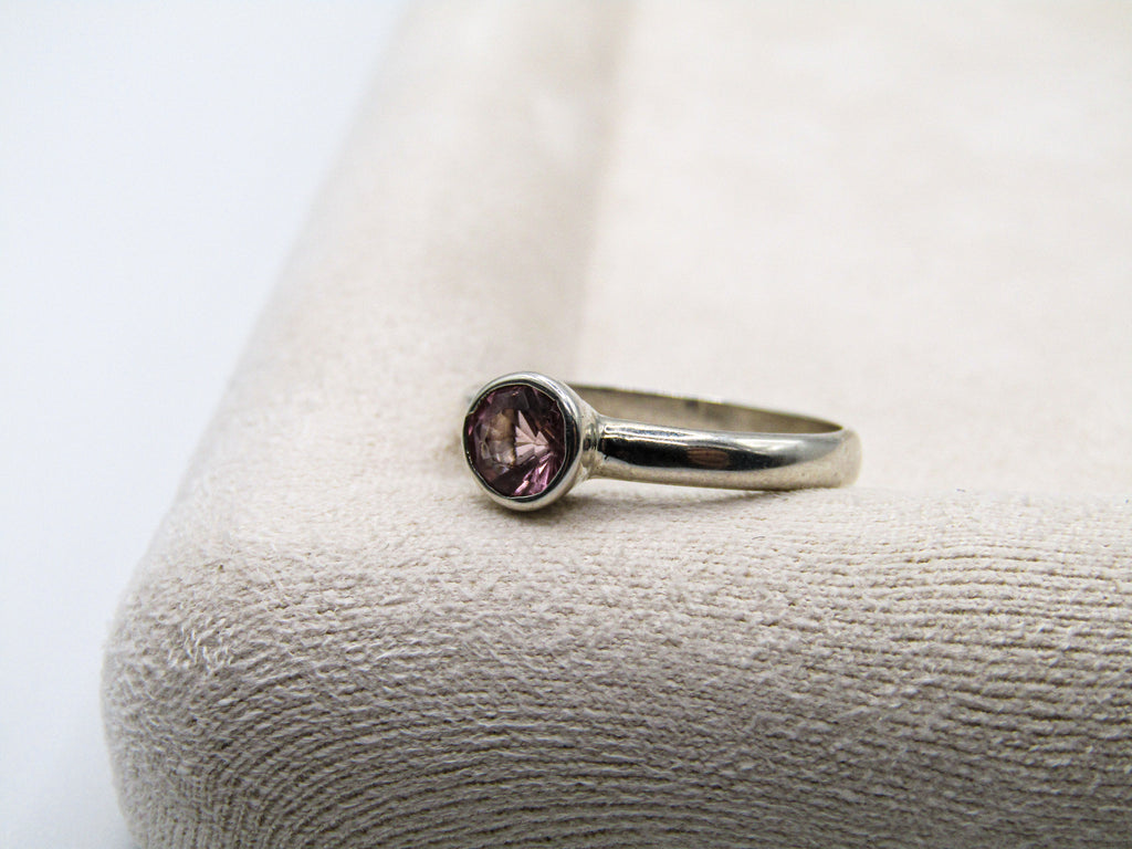 Silver ring with a purple gemstone on a textured white surface