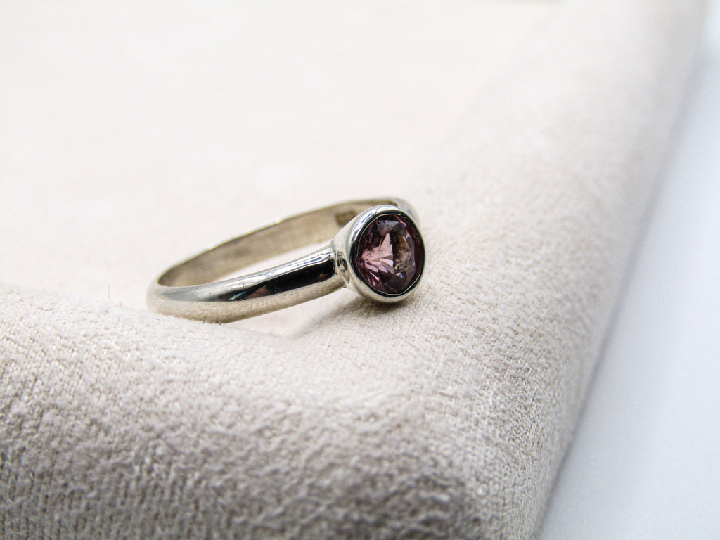 Silver ring with a purple gemstone on a textured surface