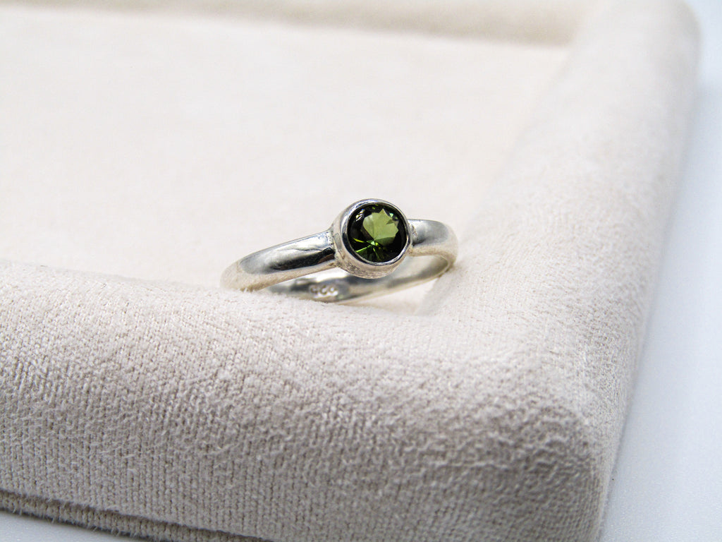 Silver ring with a green gemstone on a textured beige surface