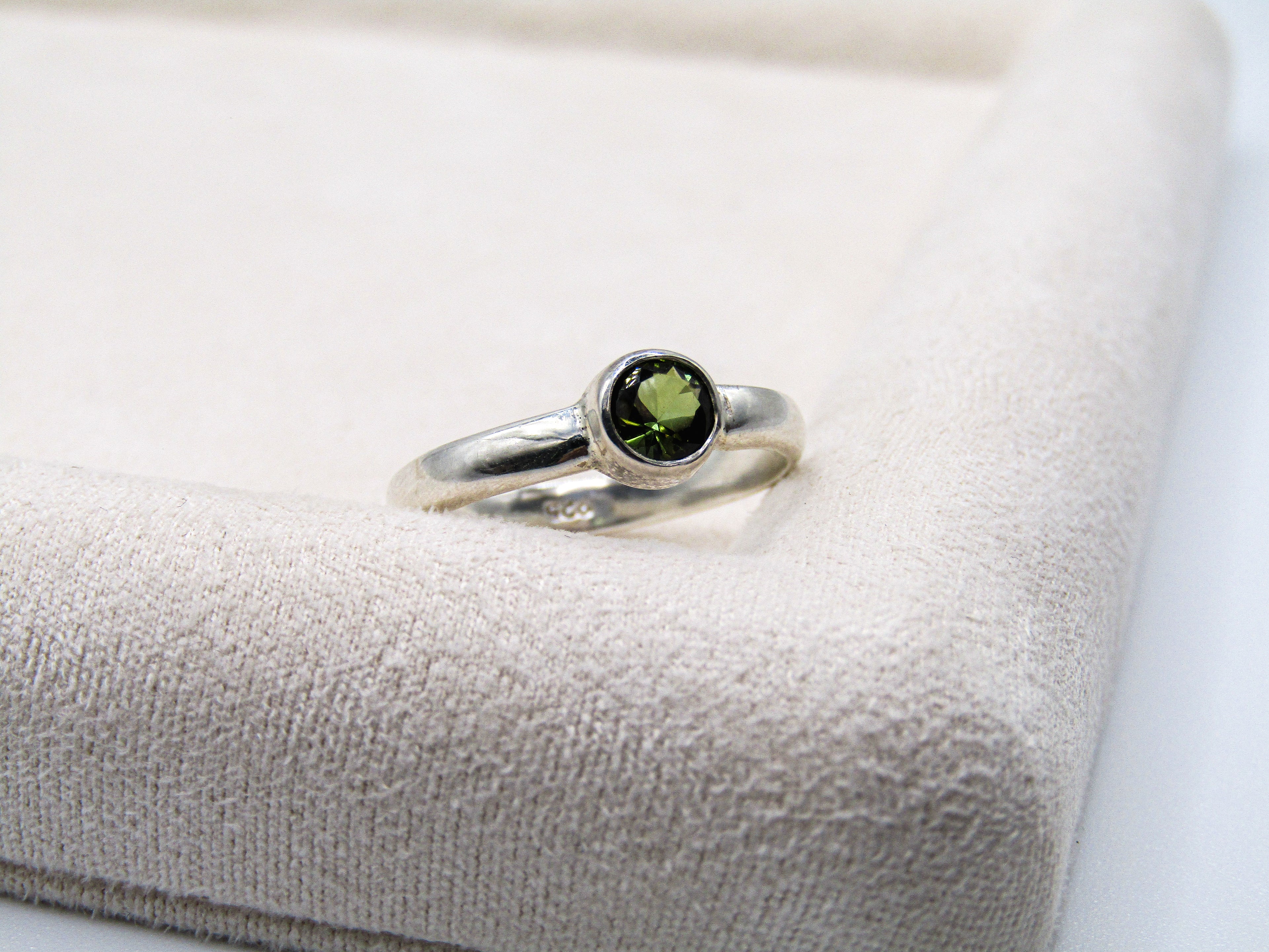 Silver ring with a green gemstone on a textured beige surface