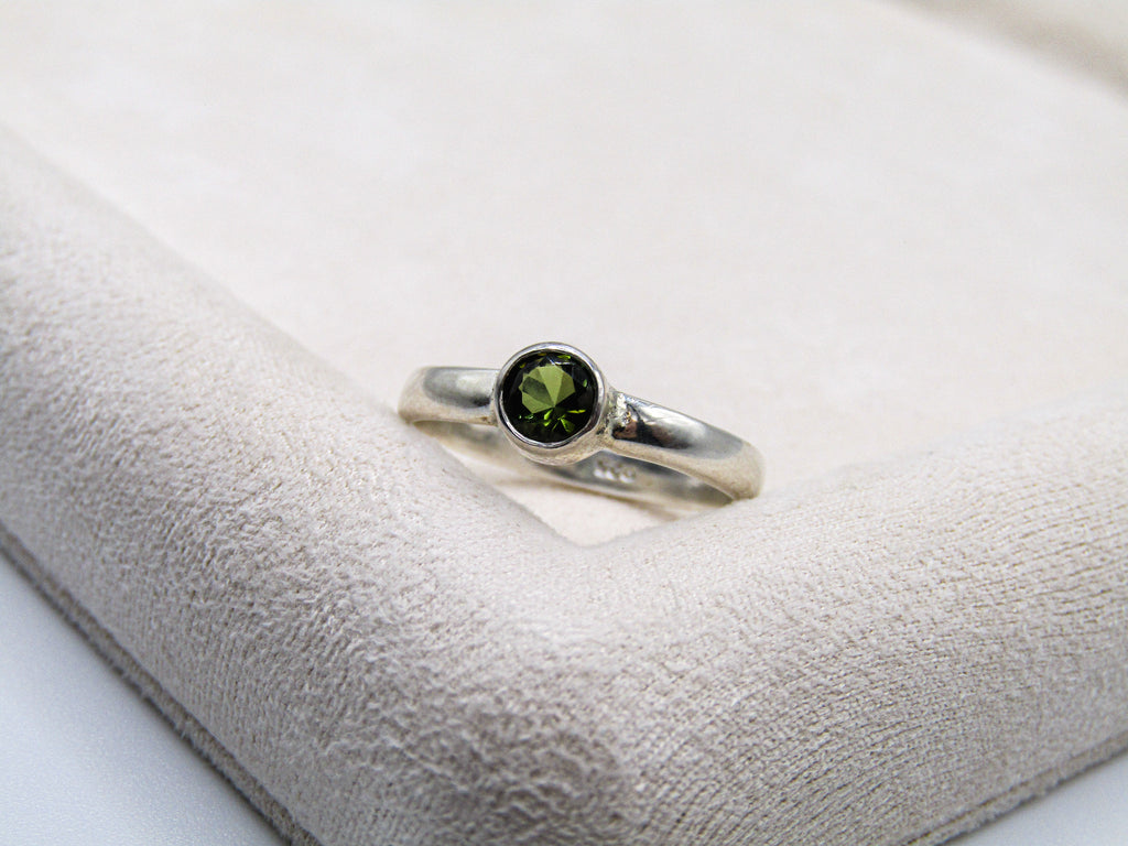 Silver ring with a green gemstone on a white cushion