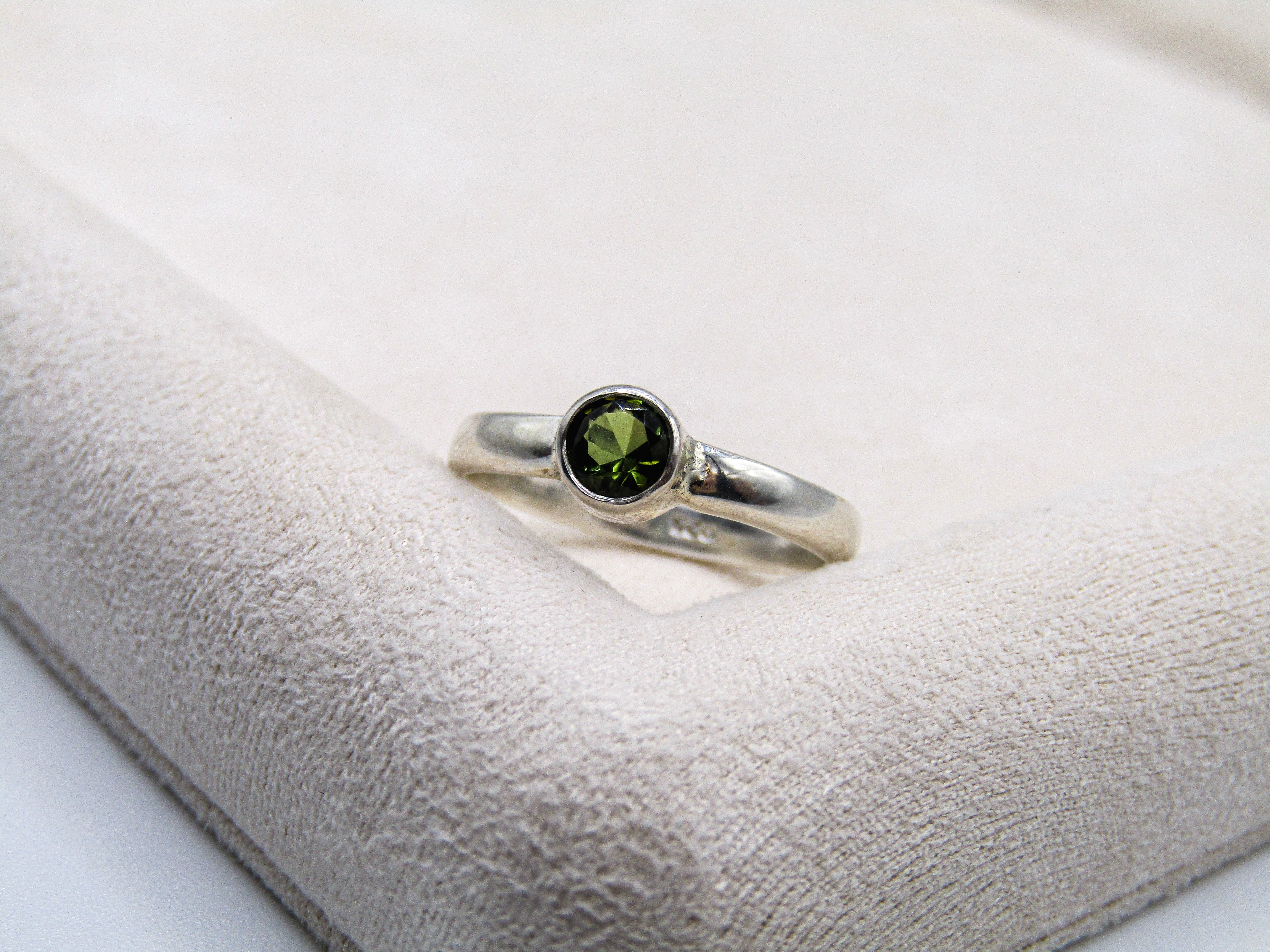 Silver ring with a green gemstone on a white cushion