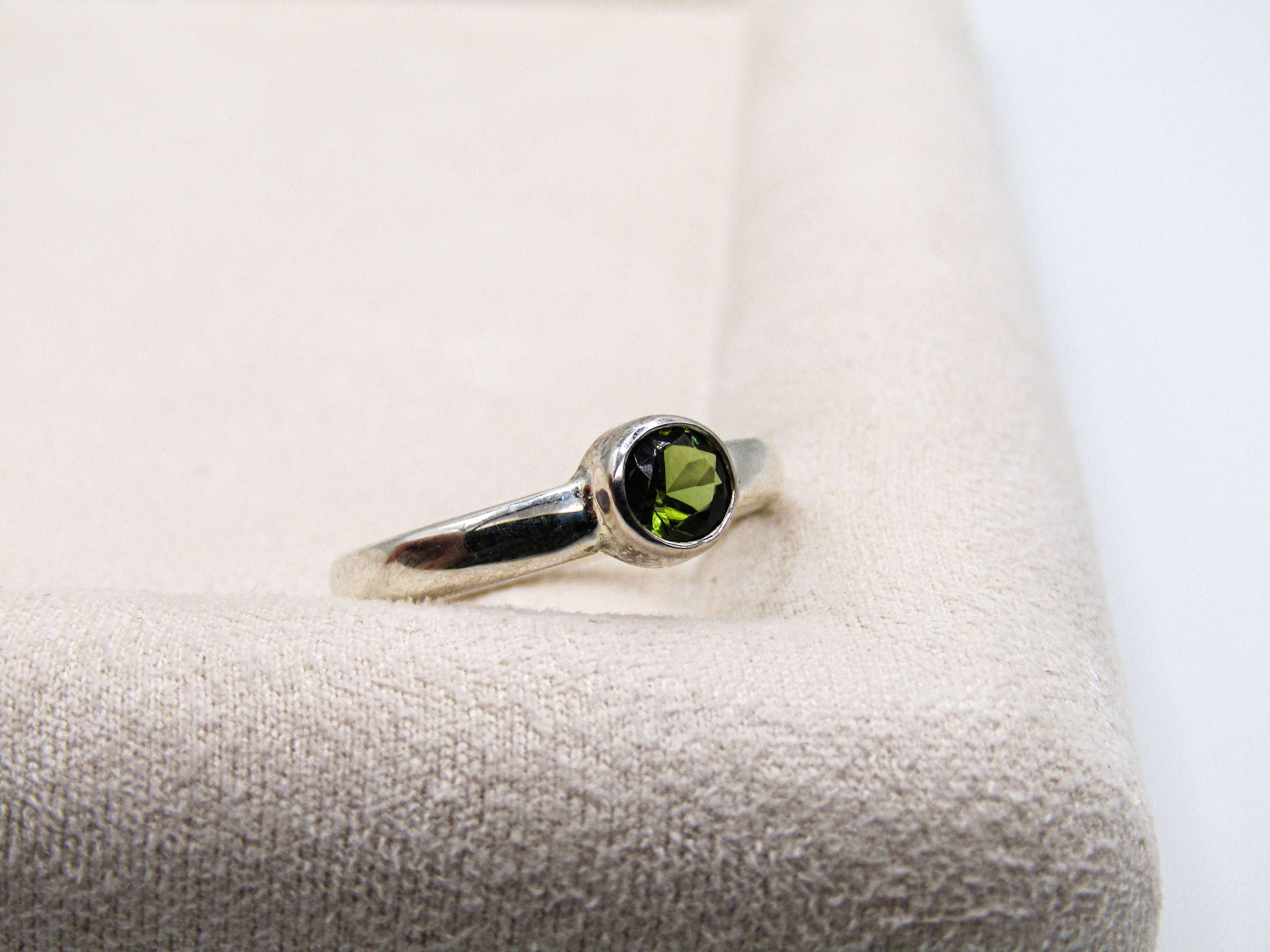 Silver ring with a green gemstone on a white cushion