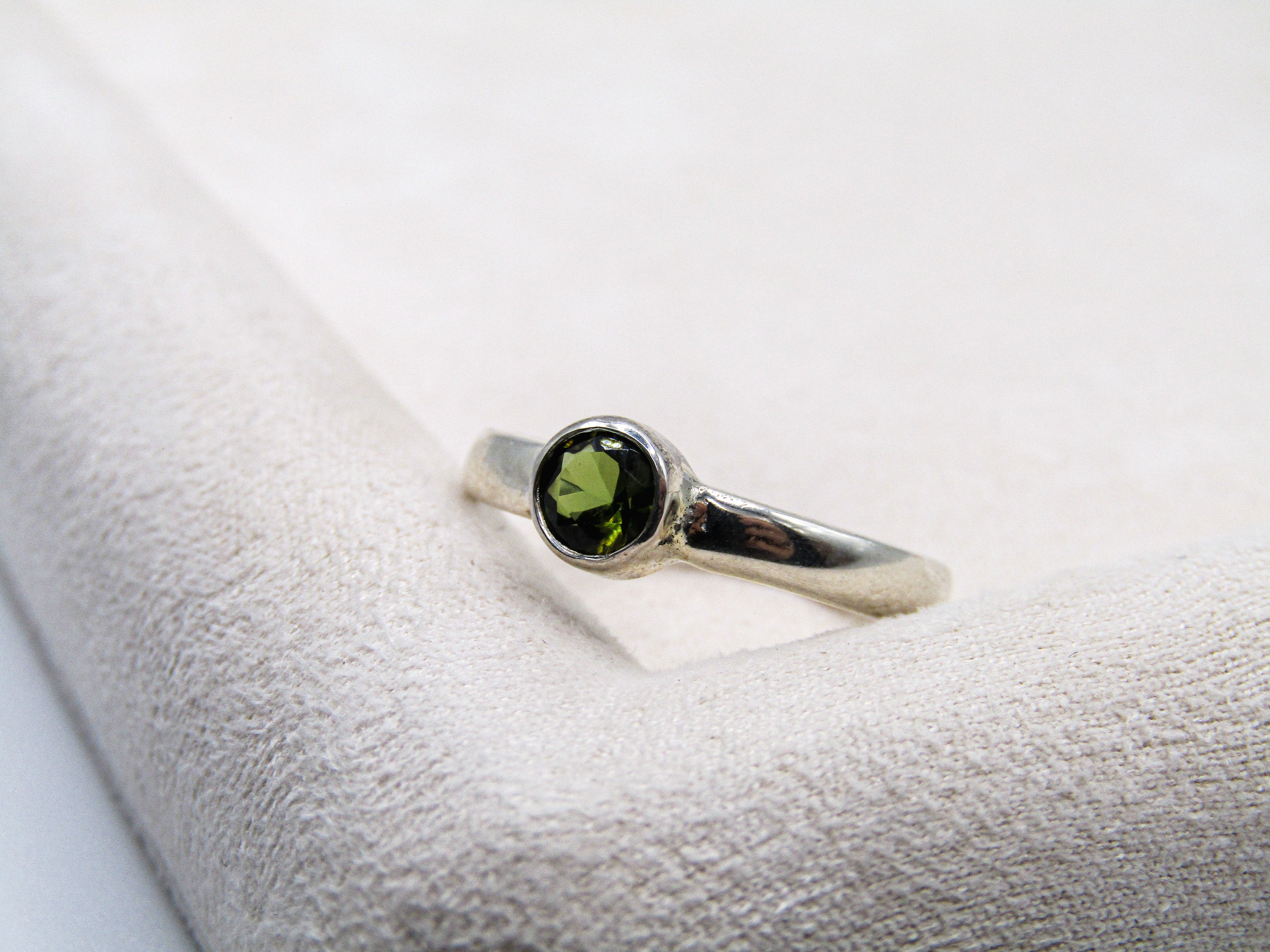 Silver ring with a green gemstone on a white cushion