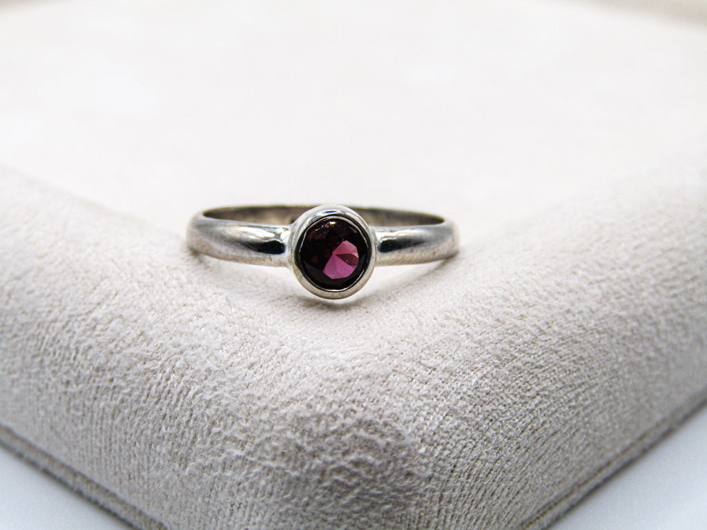 Silver ring with a red gemstone on a textured white surface