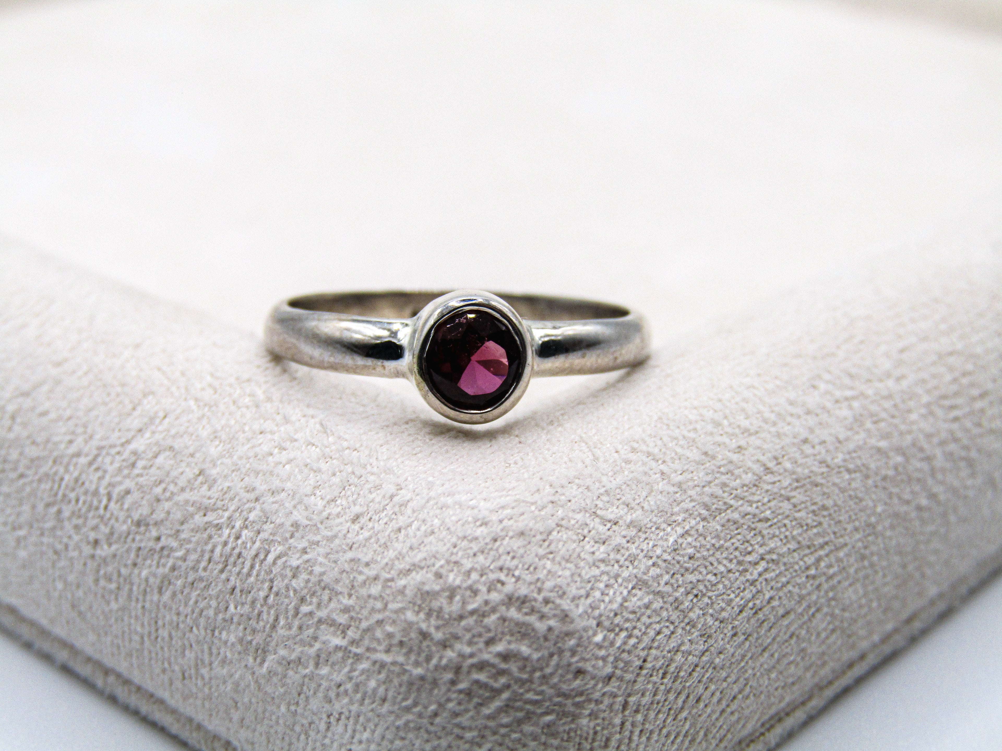 Silver ring with a red gemstone on a textured white surface