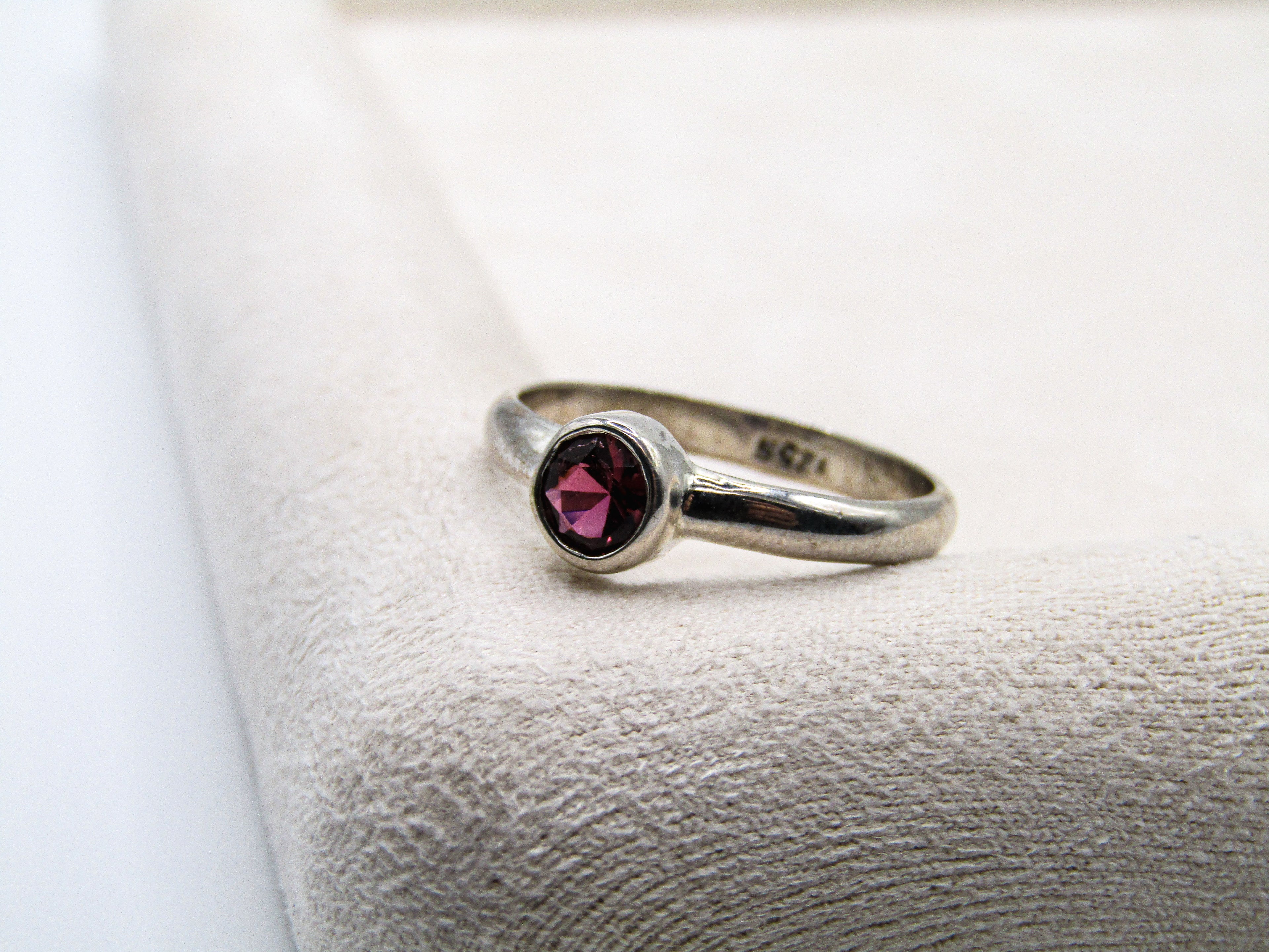 Silver ring with a red gemstone on a textured white surface