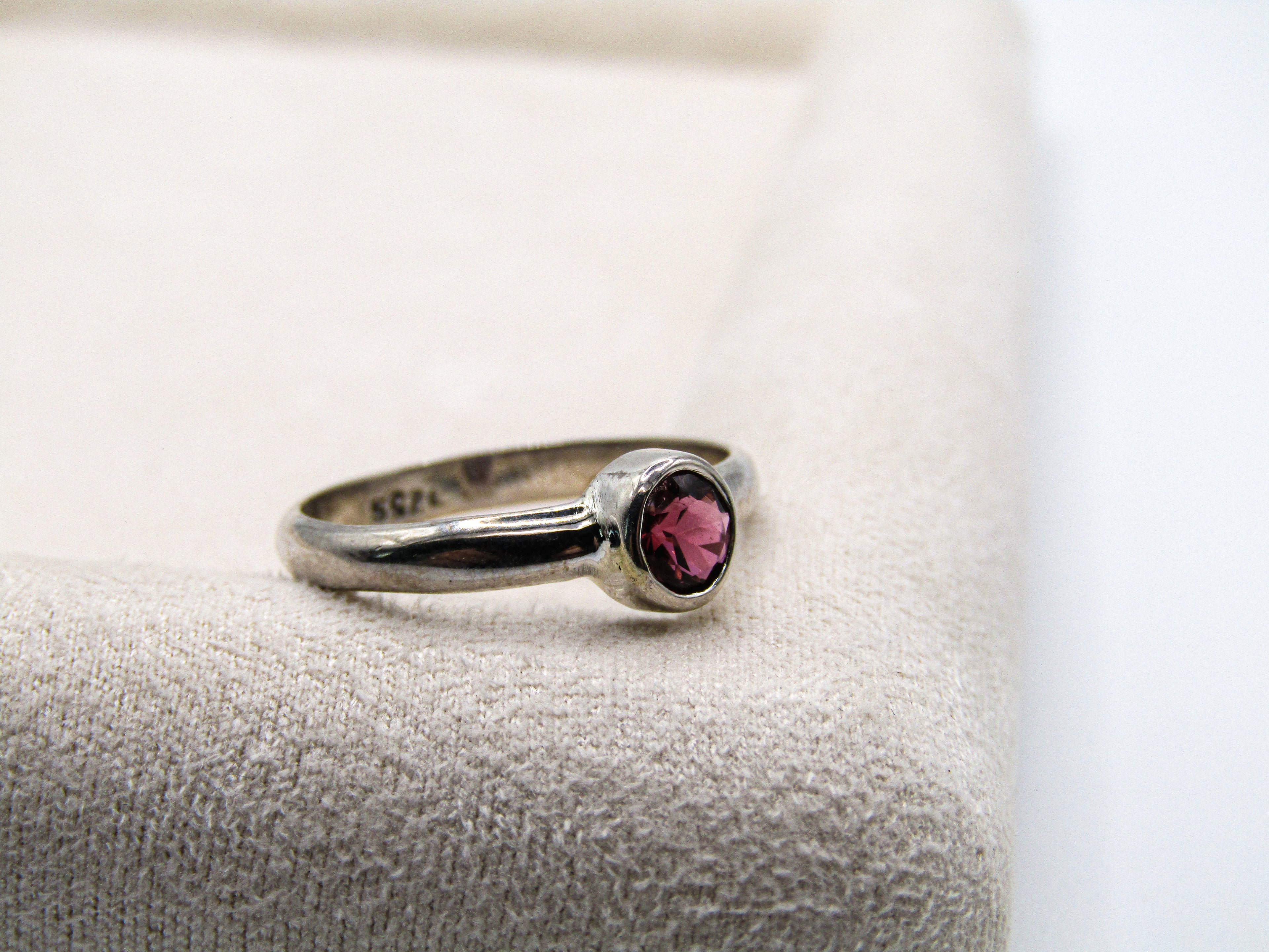 Silver ring with a red gemstone on a textured surface