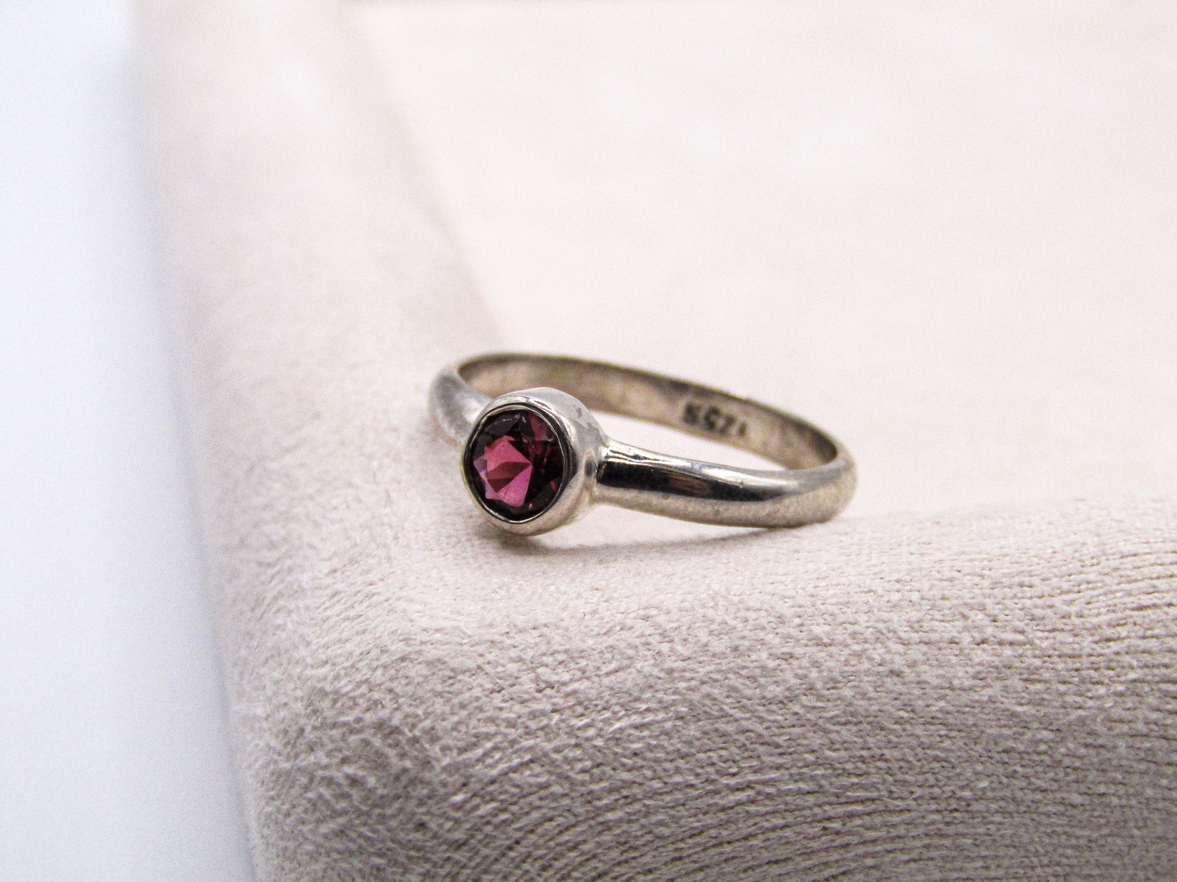 Silver ring with a red gemstone on a textured white surface