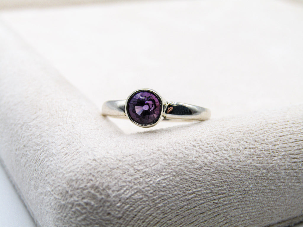 Silver ring with a purple gemstone on a white cushion