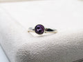 Silver ring with a purple gemstone on a white cushion