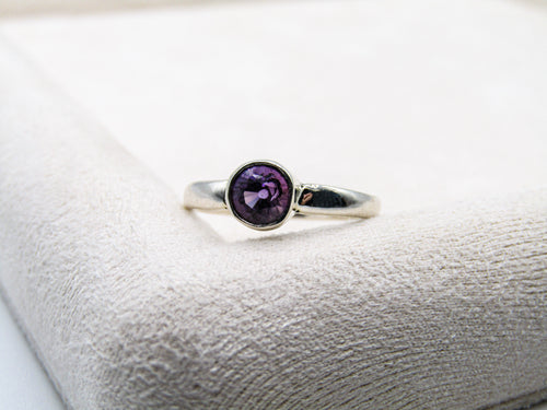 Silver ring with a purple gemstone on a white cushion