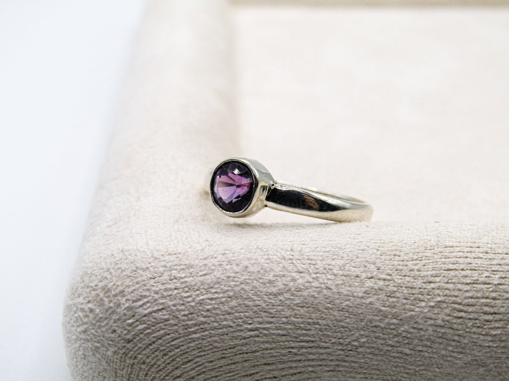 Silver ring with a purple gemstone on a textured white surface