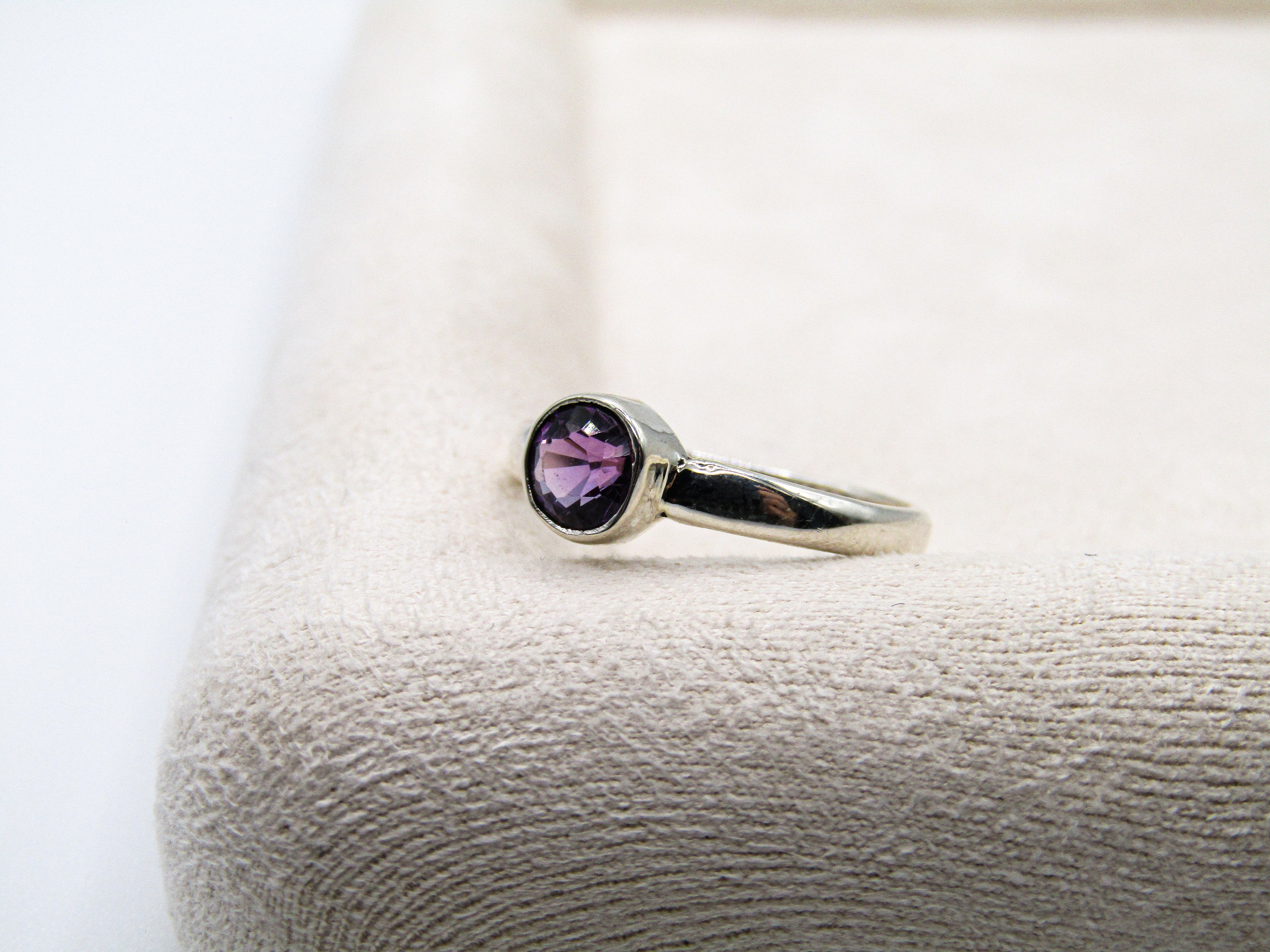 Silver ring with a purple gemstone on a textured white surface