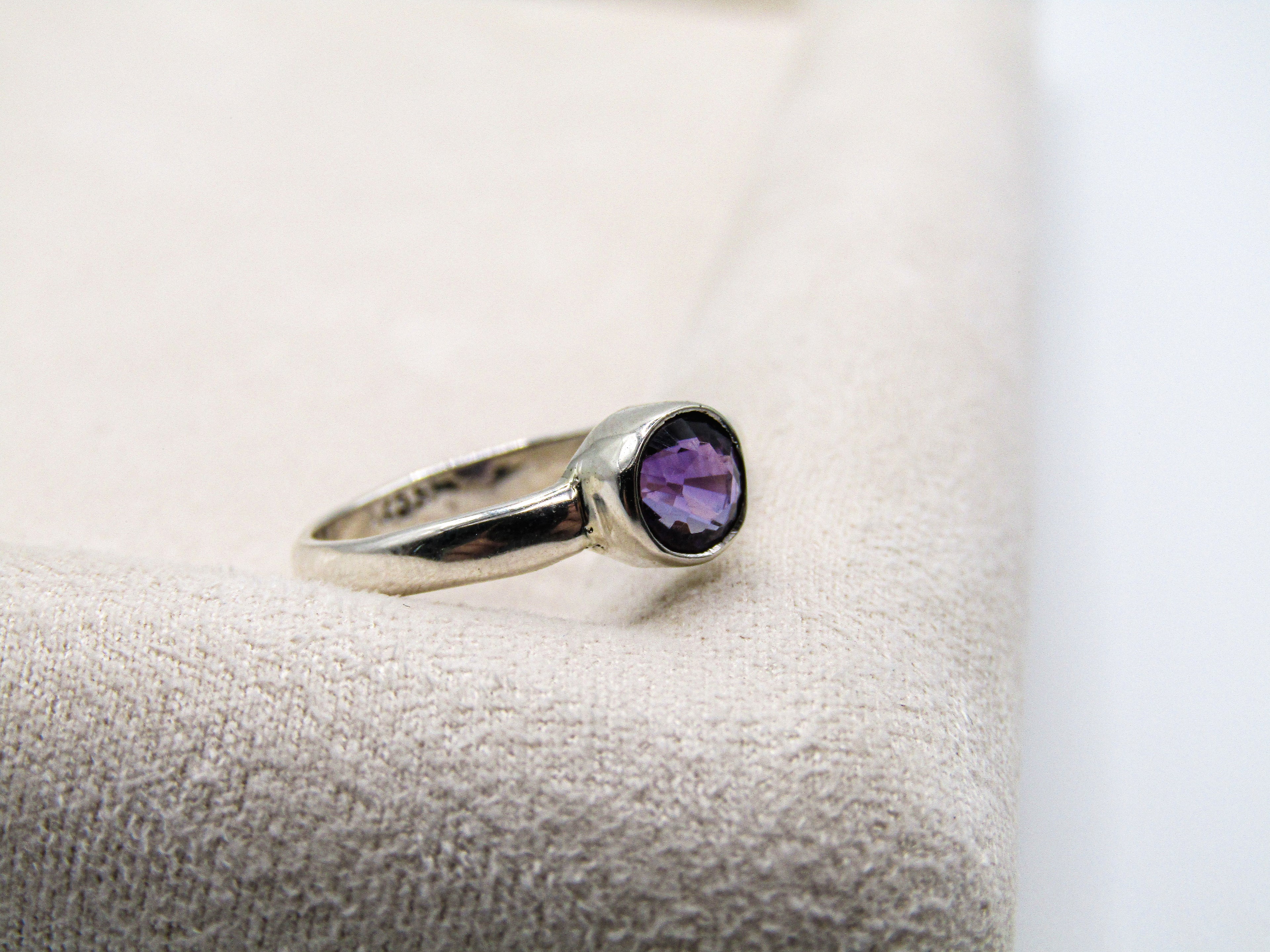 Silver ring with a purple gemstone on a textured surface
