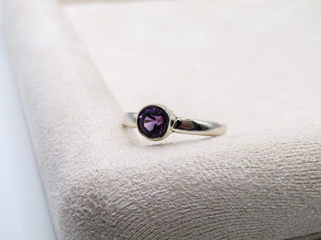 Silver ring with a purple gemstone on a textured white surface