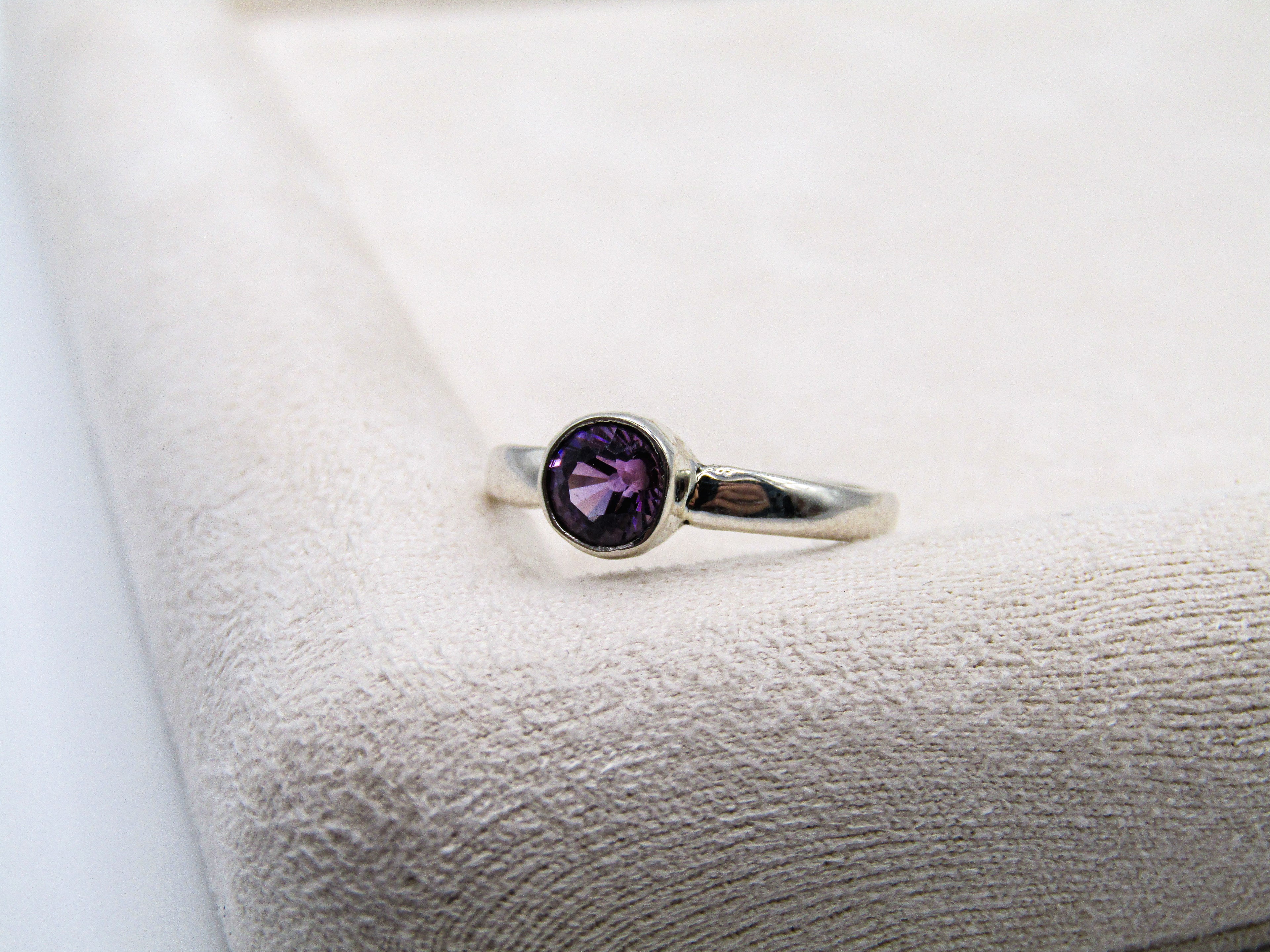 Silver ring with a purple gemstone on a textured white surface