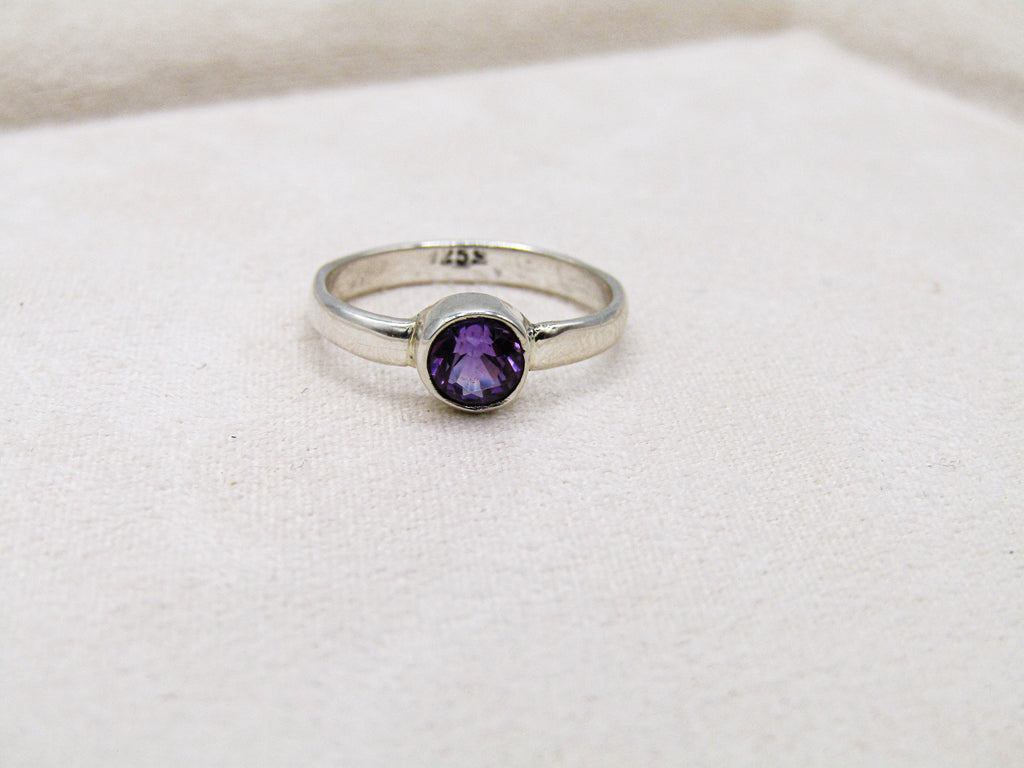 Silver ring with a purple gemstone on a white fabric background