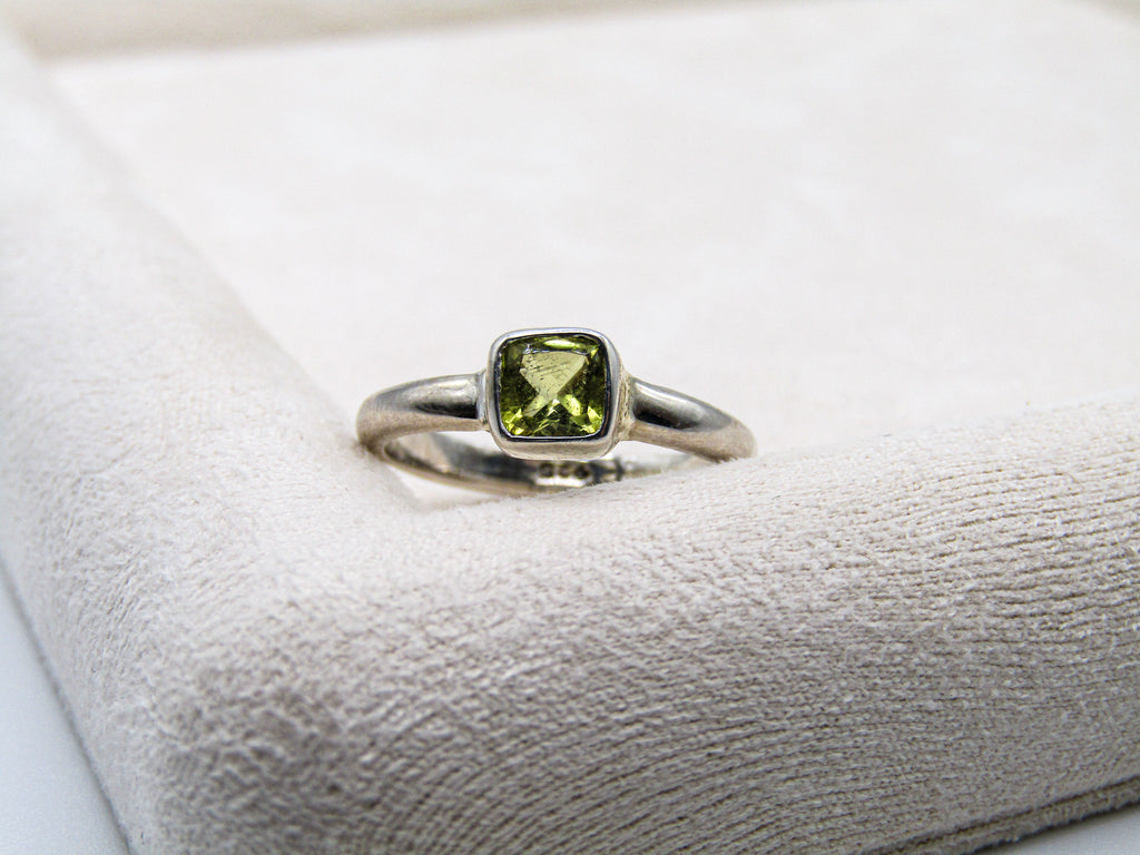 Silver ring with a green gemstone on a textured white surface