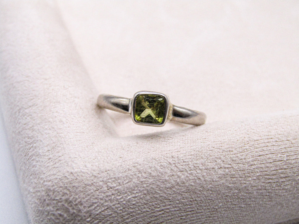 Silver ring with a green gemstone on a textured white surface